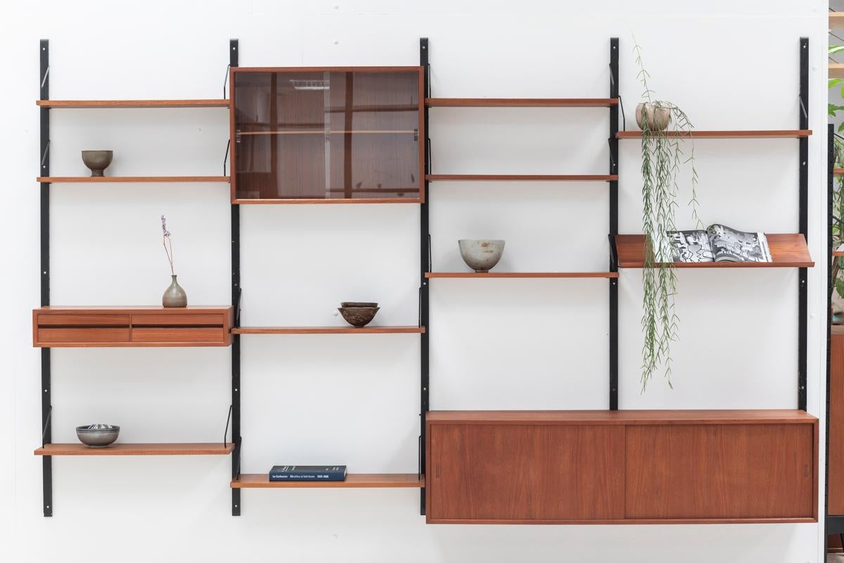 A 4-bay wall unit designed by Poul Cadovius and produced in Denmark in the 1960s. This shelving unit in teak wood is a modular system which allows you to hang the configuration of shelves and cabinets as desired. The set features  two shelves with a