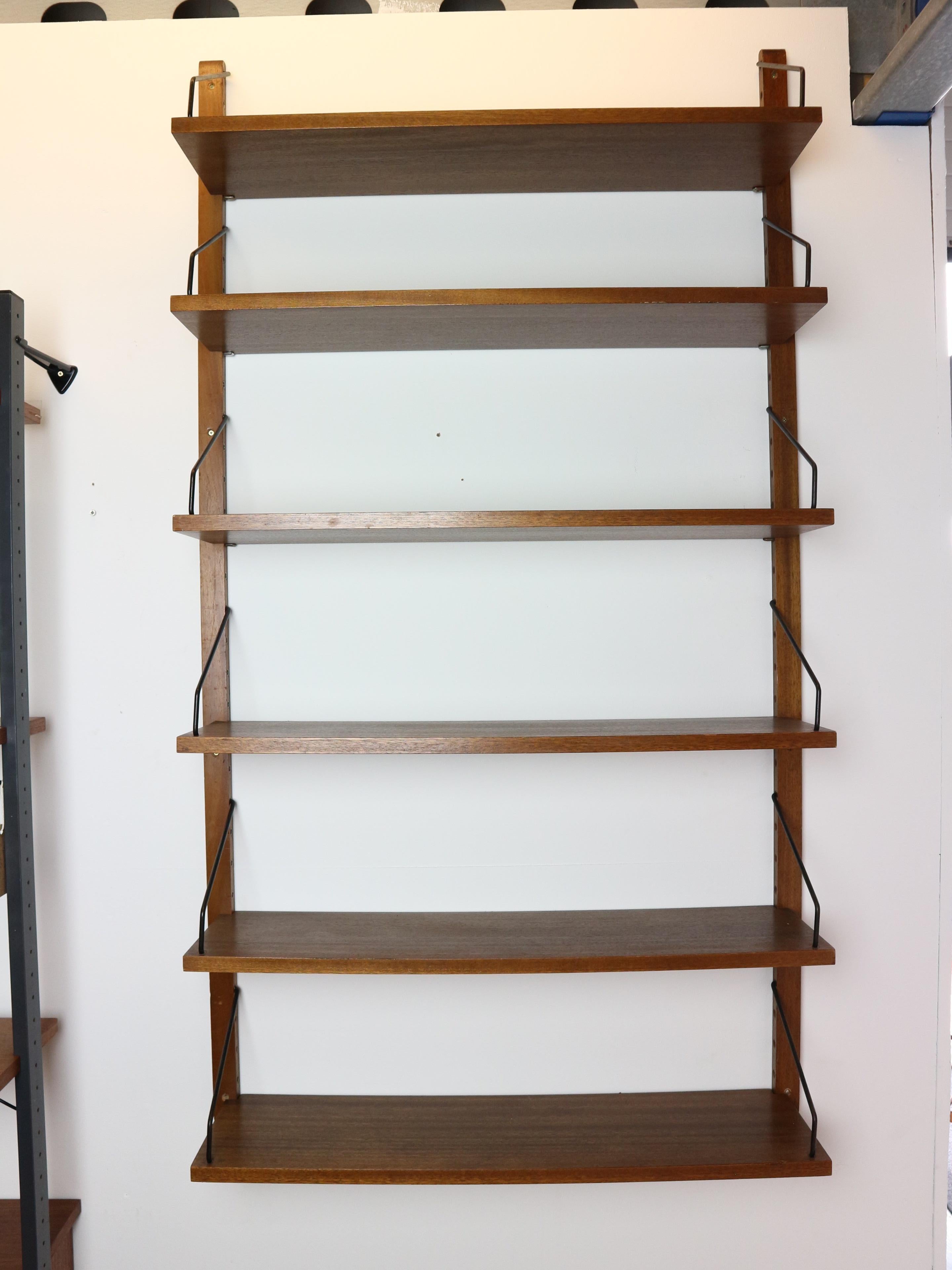 This Mid-Century walnut wall-mounted shelving system, made by Danish designer Poul Cadovius has interchangeable shelves mounted on wooden risers and black metal paginated brackets. 
The shelf can be used for books or other decoration/objects. 
When