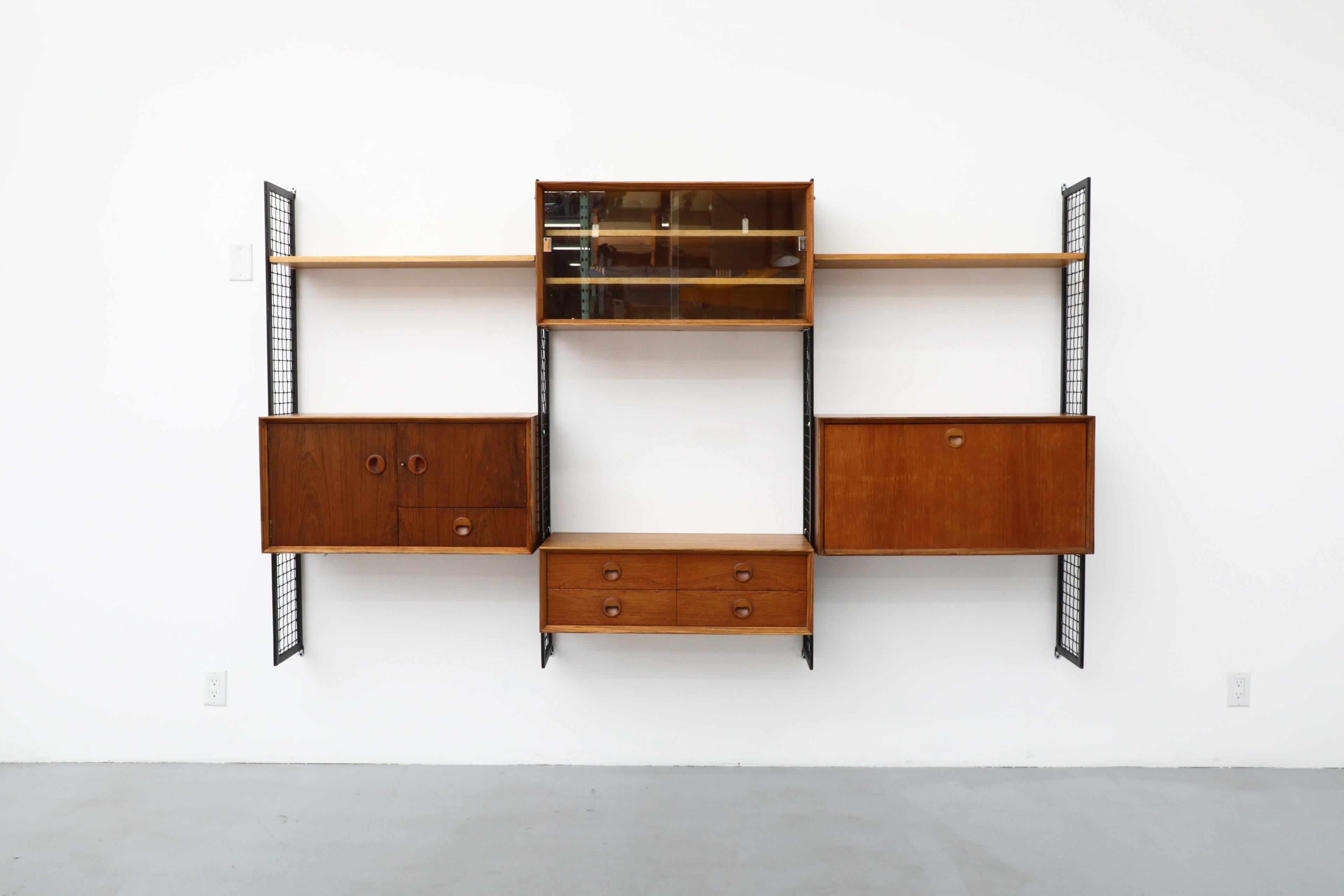 Mid-Century Zebrawood, Teak, Elm, and laminate wall unit with cabinets shelving and drawers mounted on black enameled metal grid risers. This unit is completely adjustable. There is some bubbling to the veneer in spots as well as scratches and