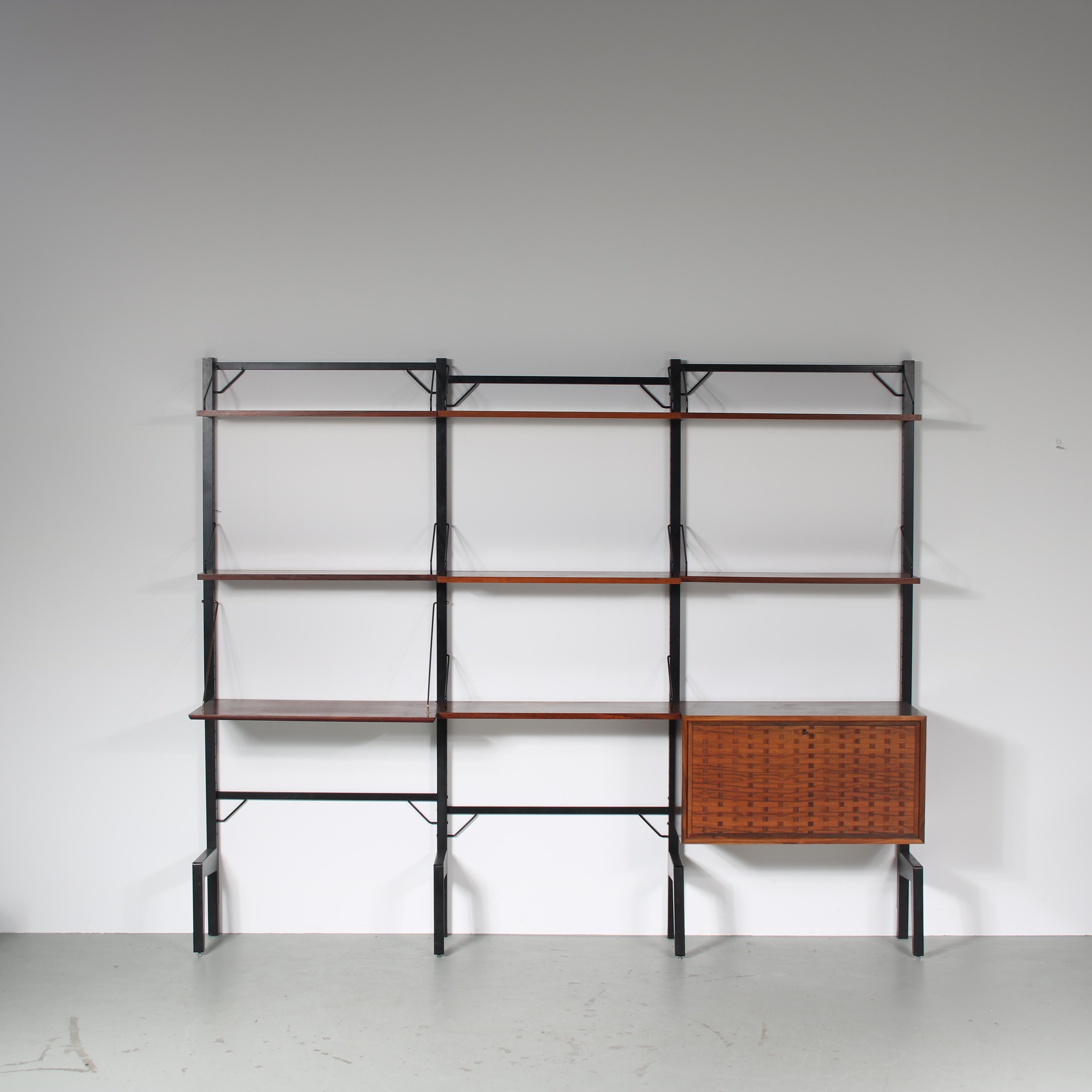 An eye-catching wall mounted system cabinet designed by Poul Cadovius, manufactured by Royal System in Denmark around 1960.

A beautiful piece made of wood in a warm brown colour. It is three units wide, having multiple shelves held by elegant black