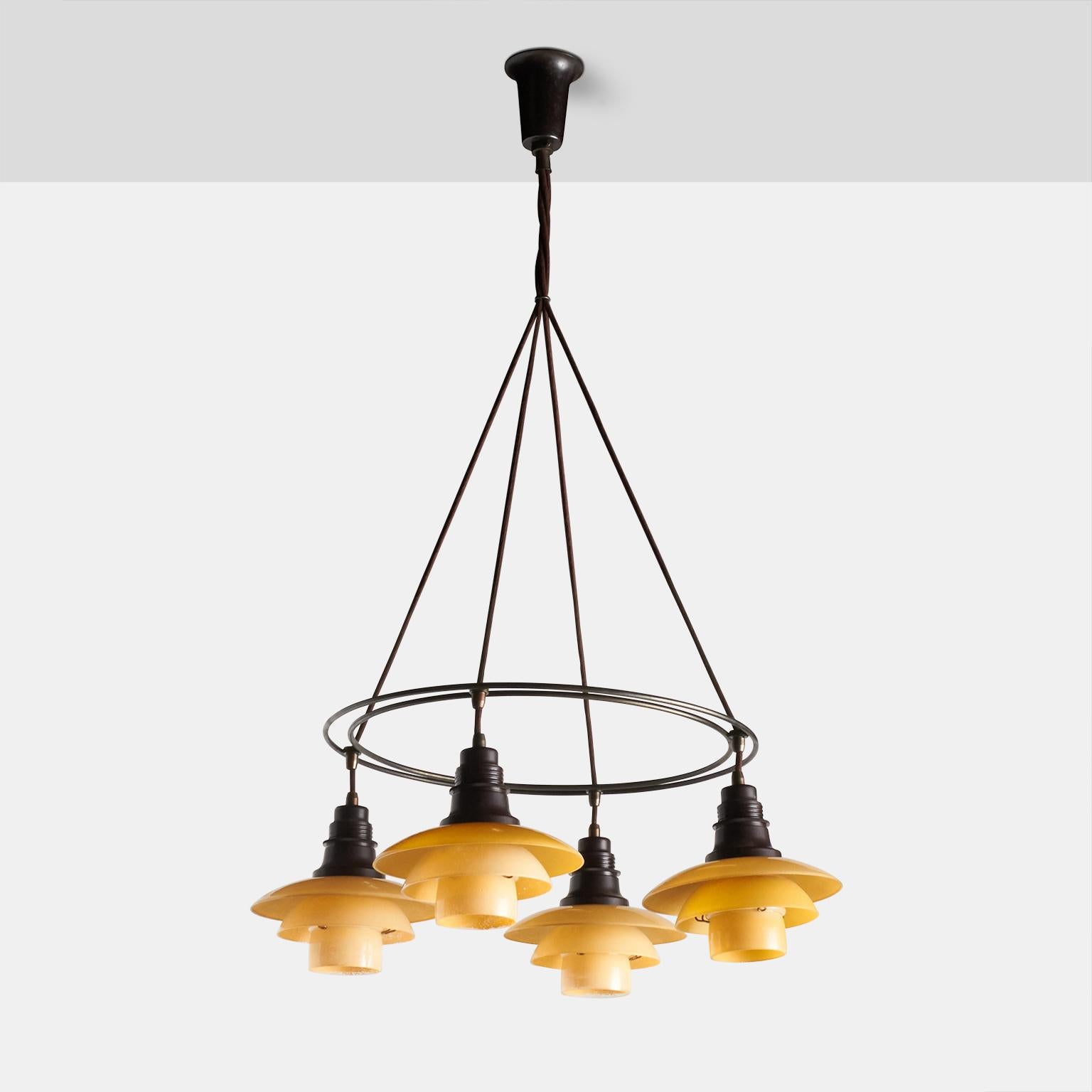 A double ring chandelier by Poul Henningsen. Features a browned brass frame, four shades of 2/2 yellow/matte glass with bakelite socket covers and wire holders. Stamped 
