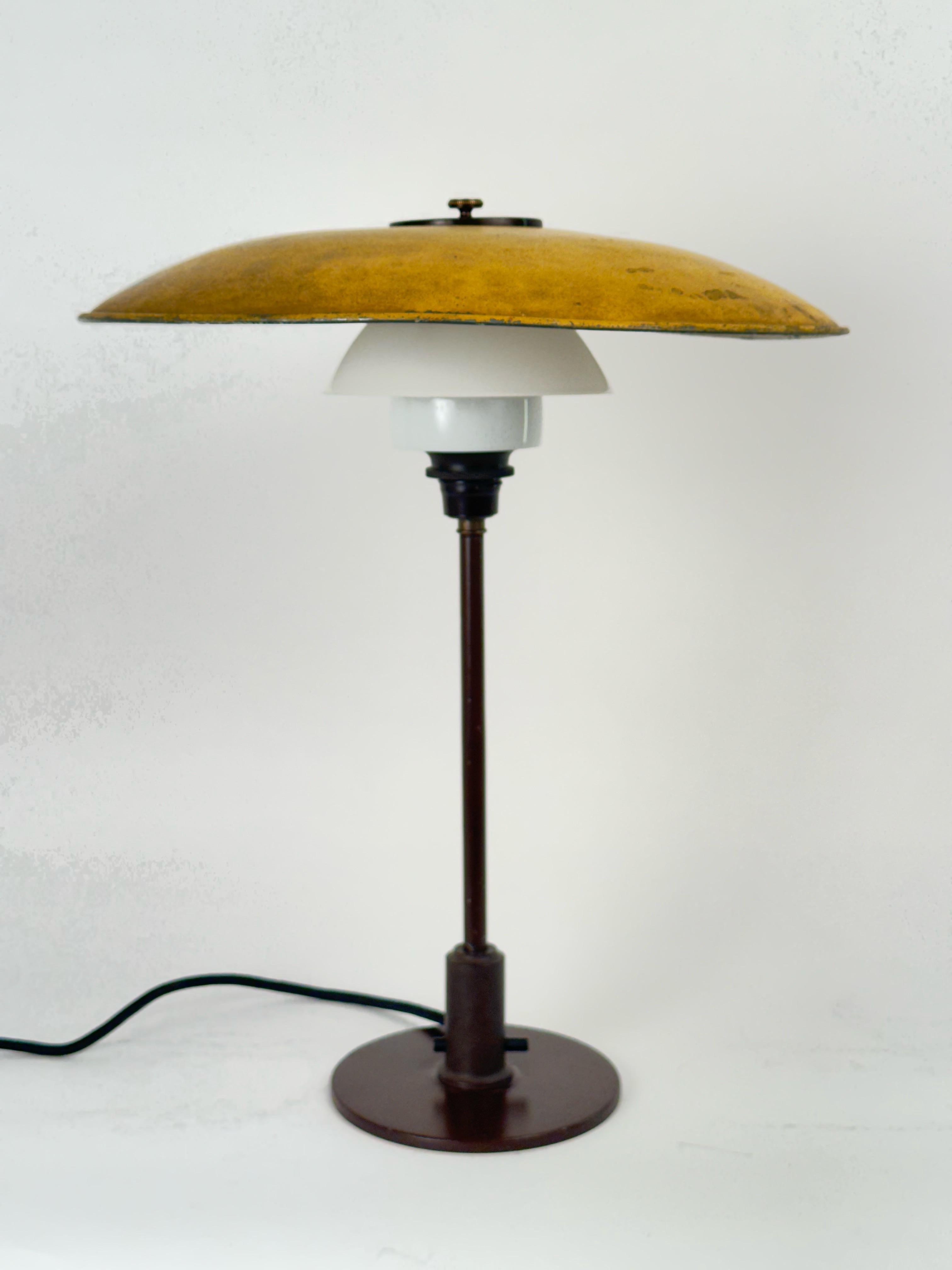 A Poul Henningsen table lamp. edited by Louis Poulsen. Brown painted iron base, burnished brass stem and top bakelite socket house and switch house. Continous switch button. Zinc upper shade, three-layer opal glass middle and botton shades. Entirely