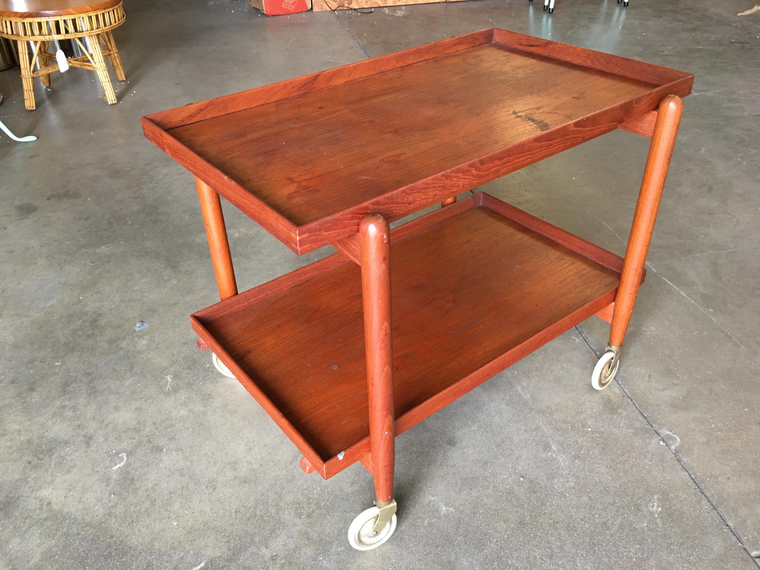 Vintage Poul Hundevad Danish Modern teak rolling bar cart. The ingenious design allows you to slide the top shelf to the left, lift the bottom shelf, and add it to the top to create a double-wide serving tabletop surface.

This design is widely