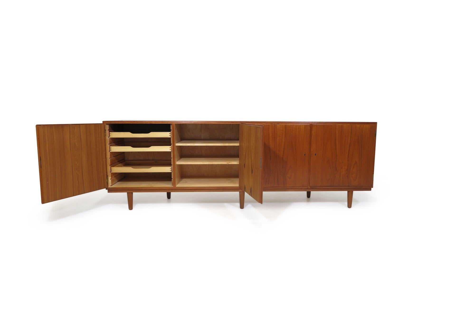 Mid-century Danish teak cabinet designed by Poul Hundevad with four locking book-matched doors opening to reveal an interior of beech with adjustable shelves and three silverware drawers on left side. The cabinet is raised on tapered legs.