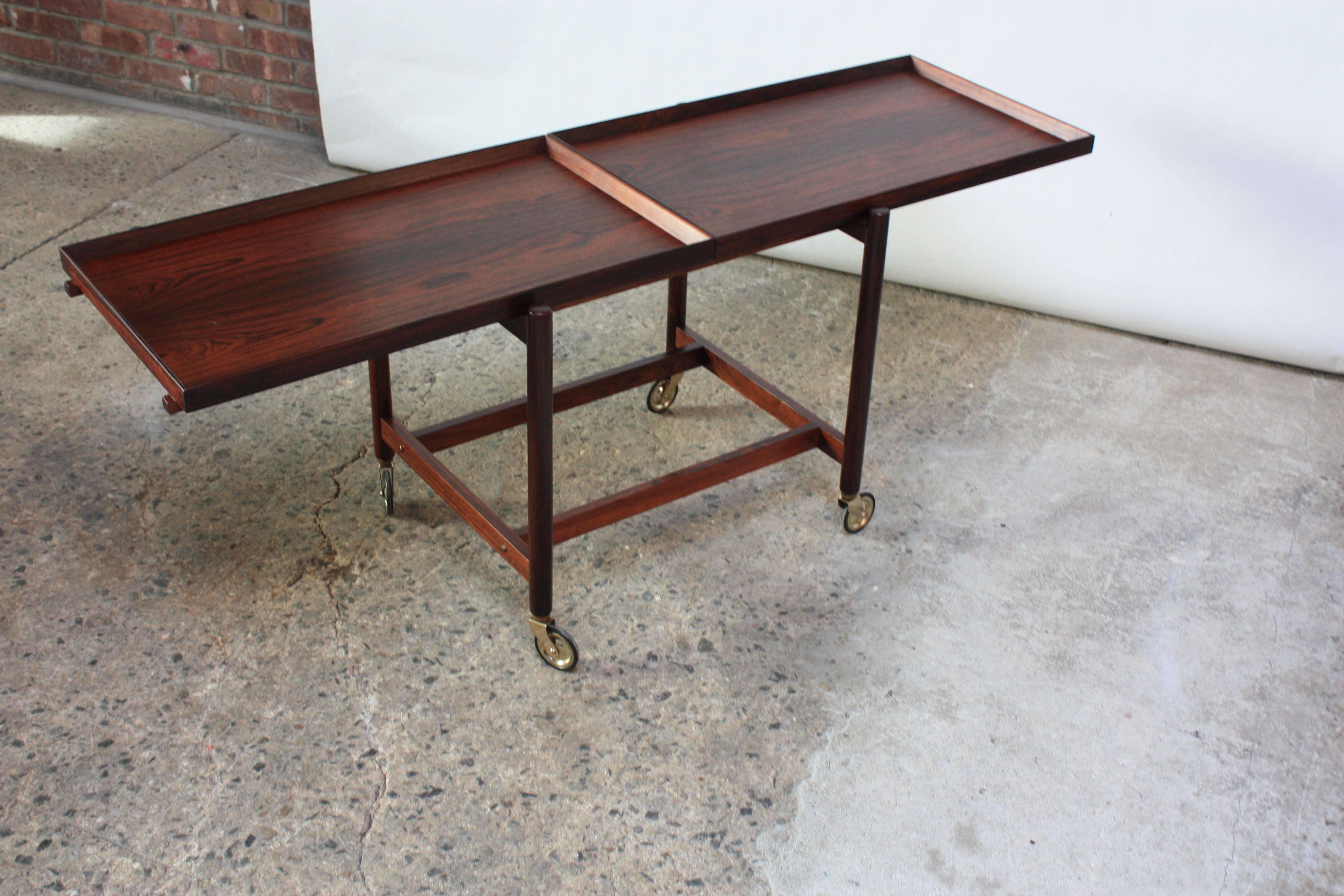 This versatile 1960s Danish modern rosewood bar cart has two functions: The piece can be assembled in a standard bar cart fashion (two, symmetrical tiers) or the bottom tier can be removed to form a longer surface on the top. The Danish control seal