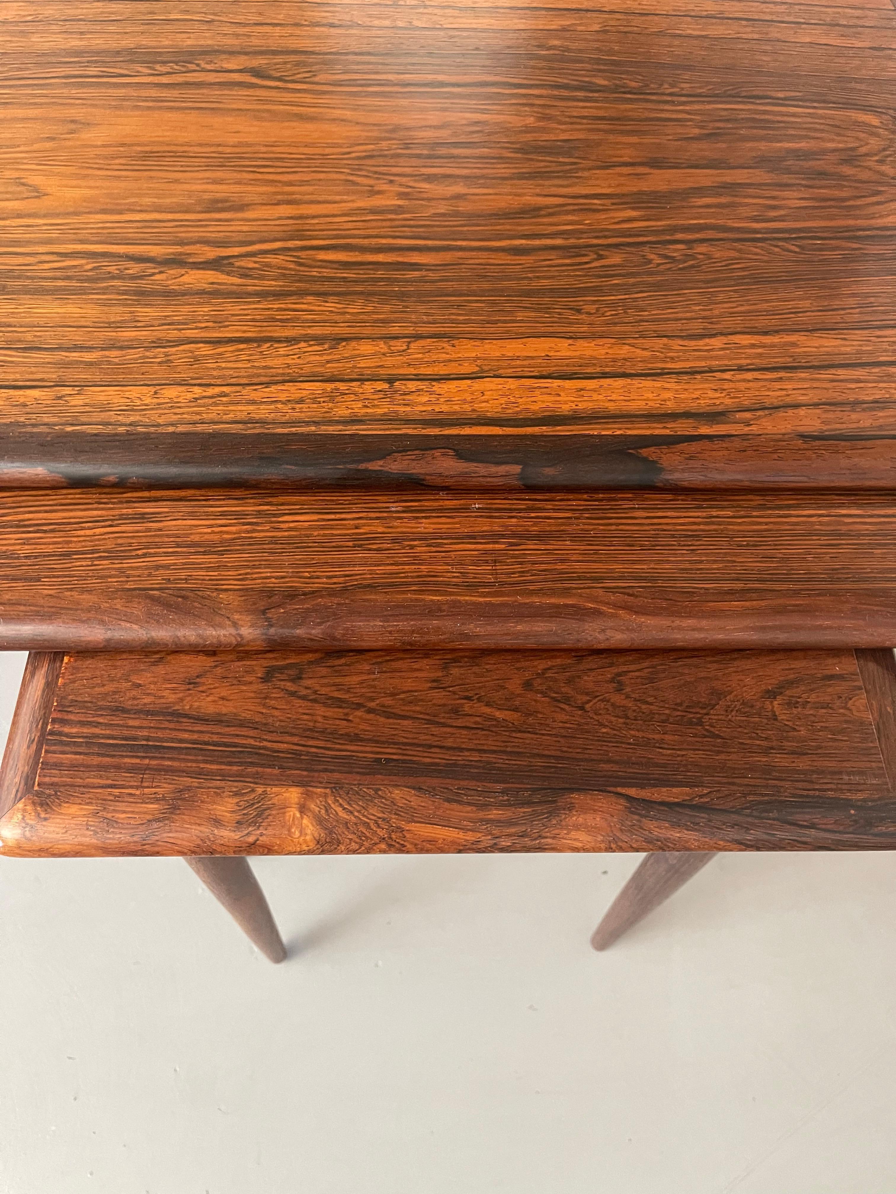 A stunning set of three nesting tables in beautifully grained rosewood. The two smaller tables slide into grooves into the larger piece. Designed by Poul Hundevad in the 1960's. They are in good age appropriate condition with some light surface