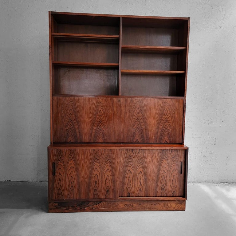 Danish modern, two piece, rosewood, bookcase secretary cabinet by Poul Hundevad features a 26 inch height bottom cabinet with sliding doors, adjustable shelves and green felt lined, pull-out drawer. The 12 inch deep, recessed top portion features