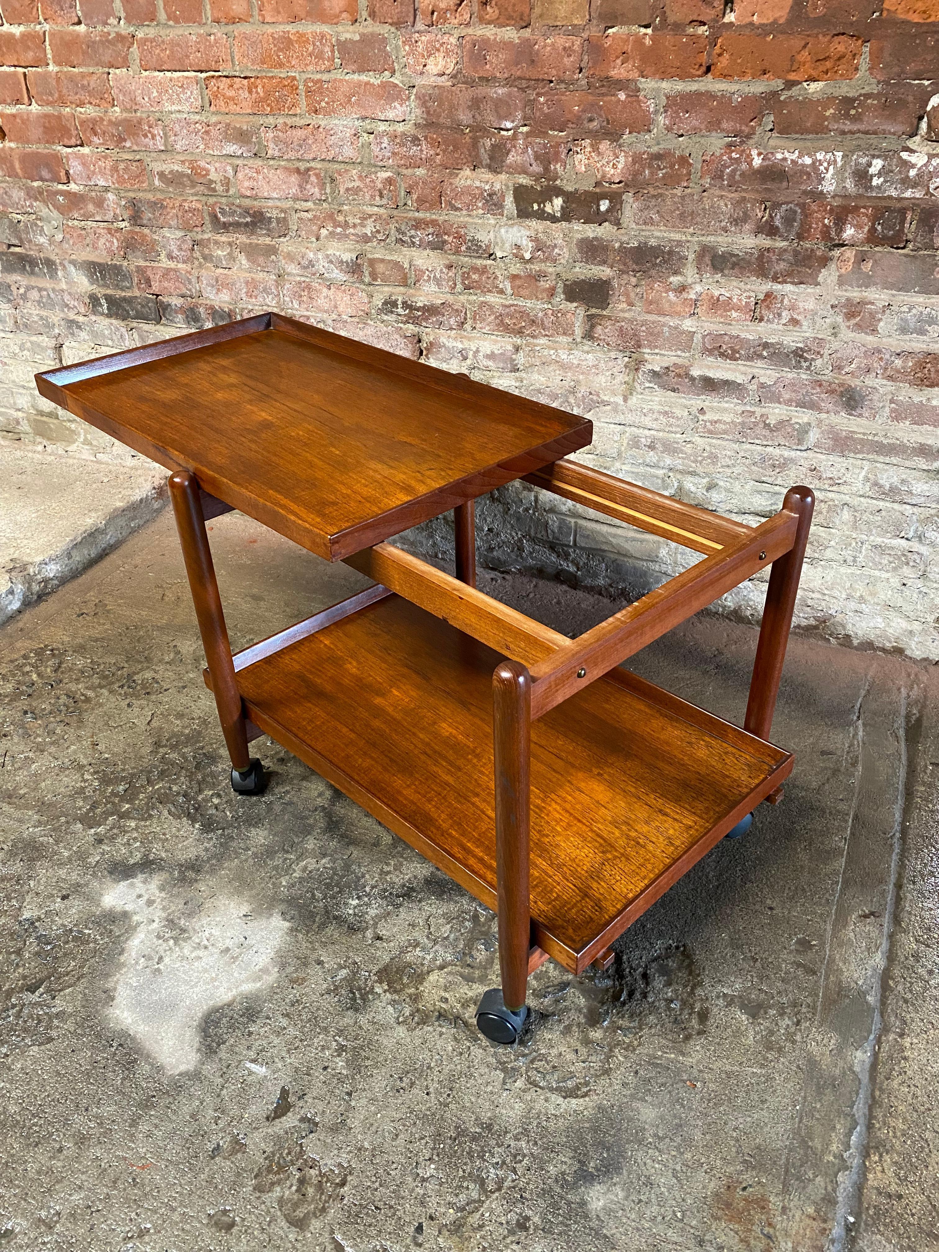 Poul Hundevad Teak rolling cart. The bottom tray lifts off and the top tray slides to make a larger display or storage area. Good practical Scandinavian ingenuity and design. Danish Control tag. 

Good overall condition with darkened oiled finish.