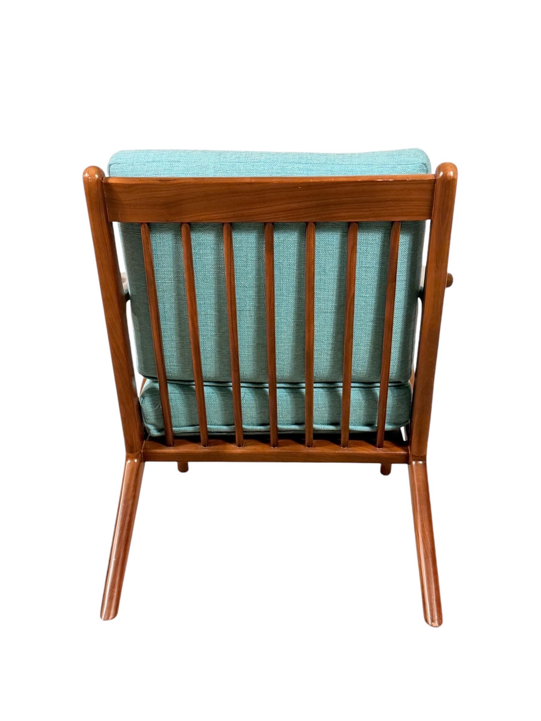This striking armchair is inspired by the iconic designs of Paul Jensen, showcasing a sleek, sculptural walnut frame that celebrates mid-century modern style. The angular arms and slatted back create a timeless silhouette, while the light blue