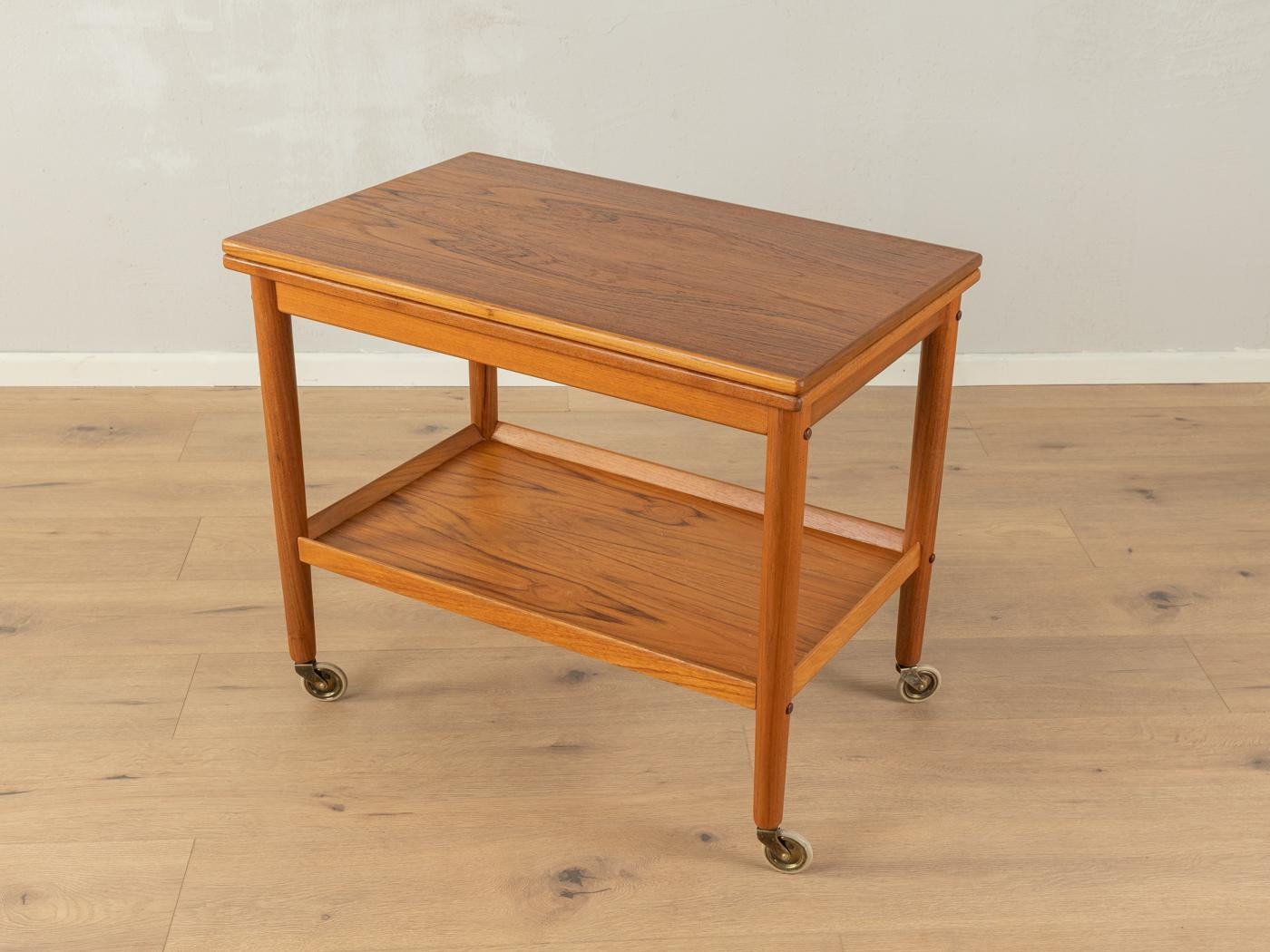 Wonderful serving trolley by Grete Jalk for Poul Jeppesen from the 1960s. Solid teak frame with two shelves in teak veneer and brass castors. The upper shelf can be rotated by 90° and then unfolded.
Extended top shelf: 90 x 70 cm 

Quality