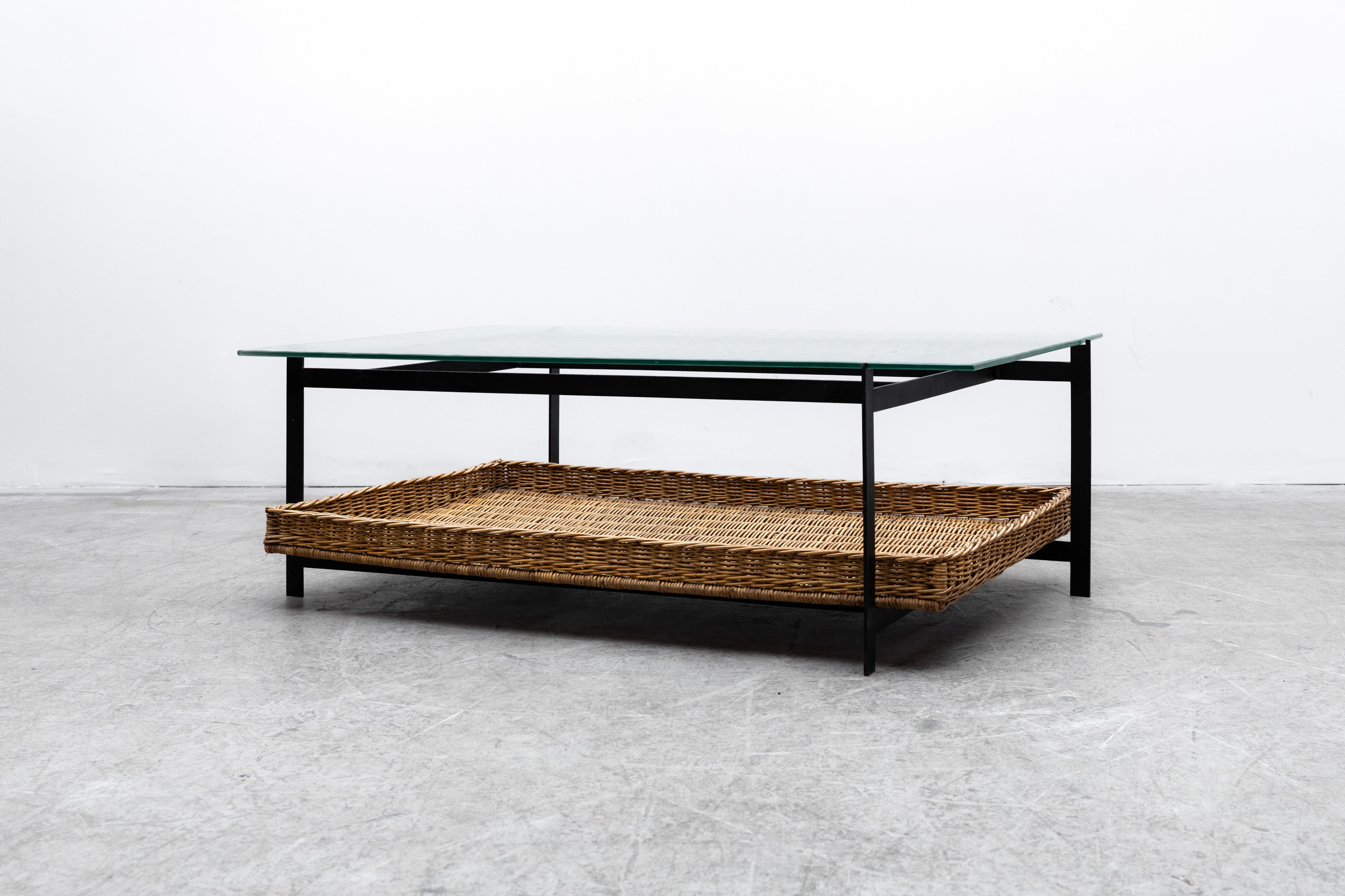 Poul Kjaerholm inspired Dutch coffee table with rattan woven basket and black enameled metal frame. In original condition with some visible scratching to glass top and enamel loss consistent with age and use.