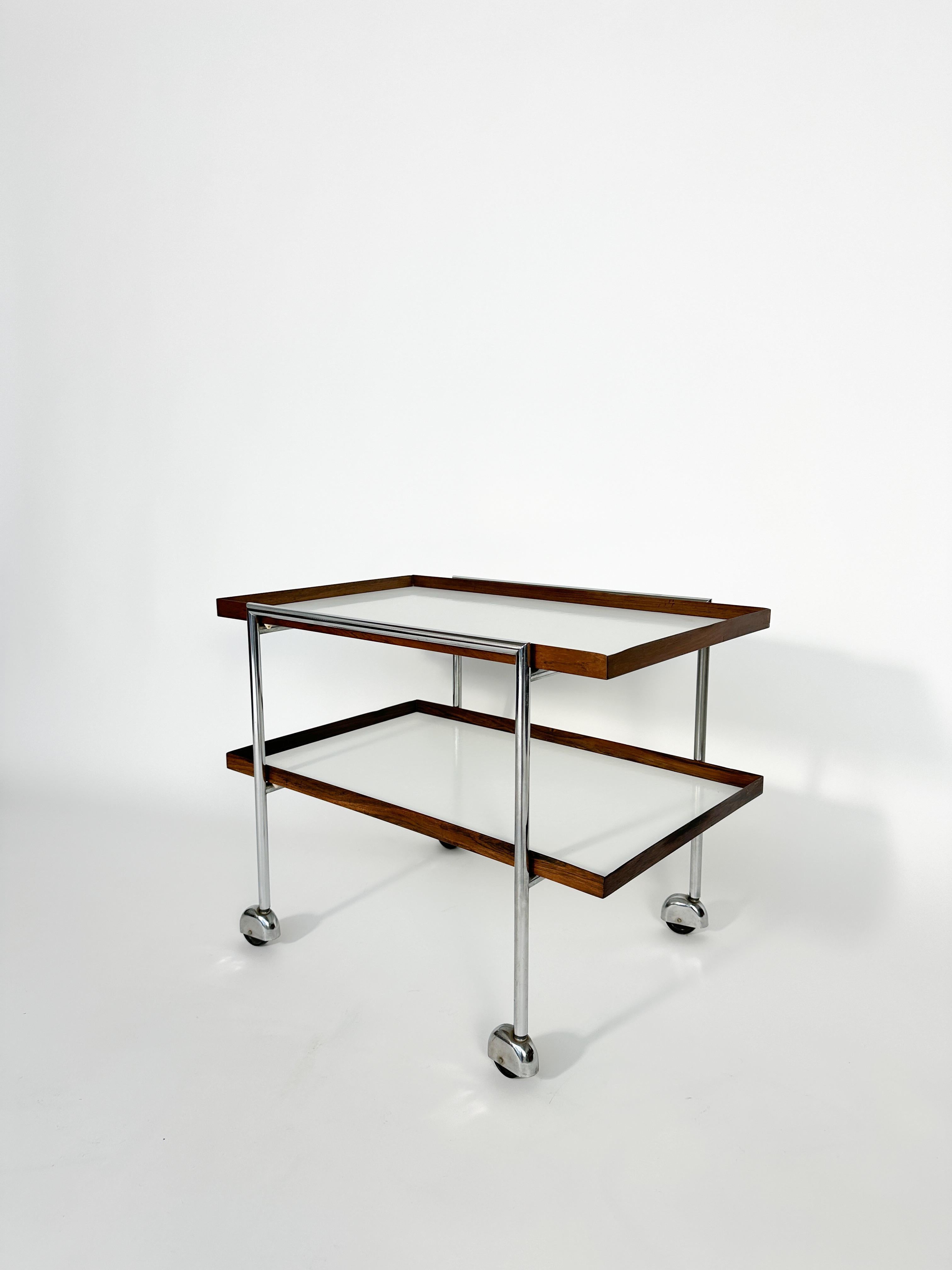 A rare Poul Nørreklit bar cart for E. Pedersen & Son, made in Denmark in the 1960s.

Chromed steel frame with rosewood framed formica trays.

Good condition with normal signs of use and age. A few spots on one of the trays, partly worn edge on one