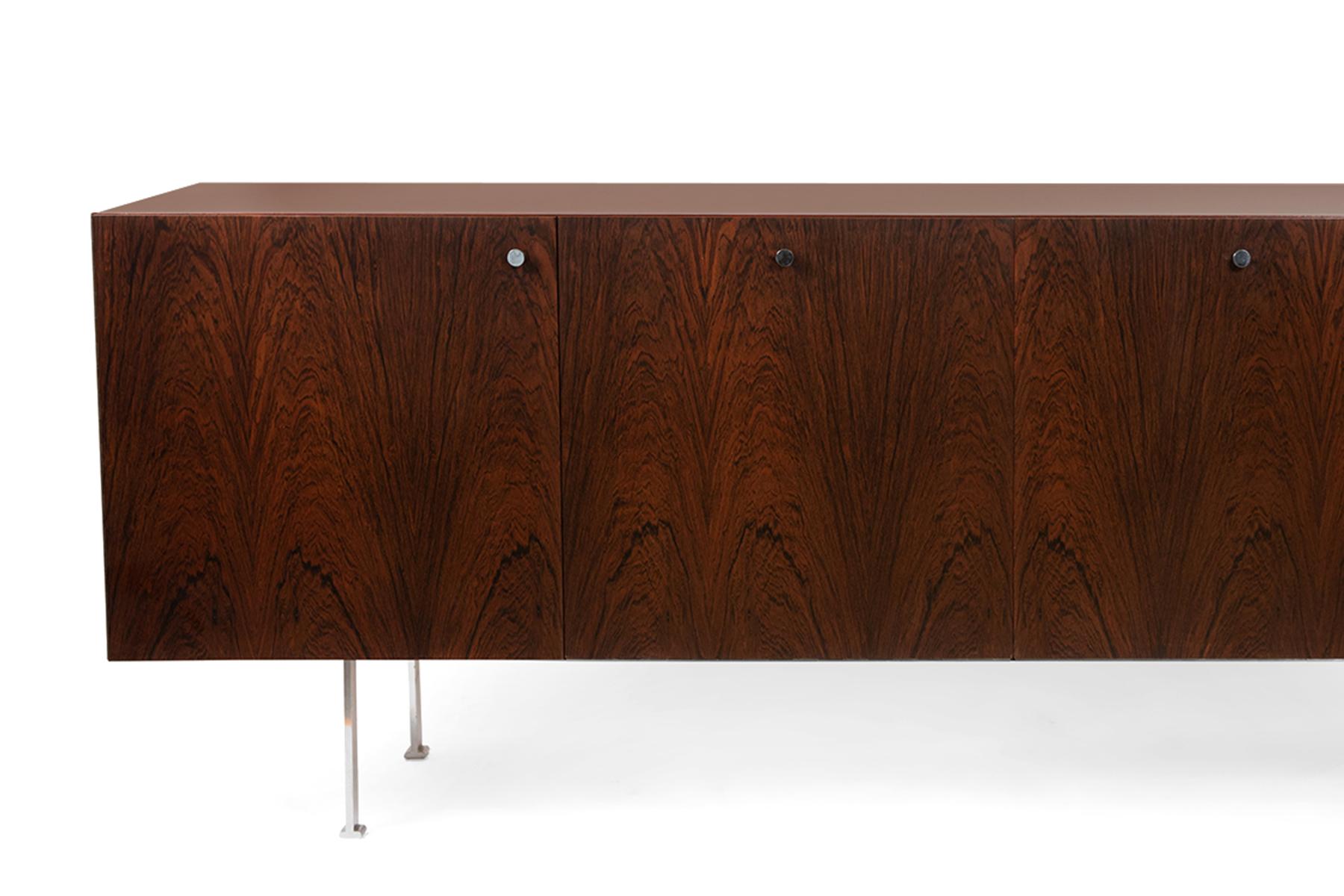 Stunning 1960s sideboard by designer Poul Norreklit featuring clean, minimalist steel legs and pulls and gorgeous bookmatched rosewood. Interior of the credenza is oak with adjustable oak and milk glass shelves and drawers. Newly refinished.