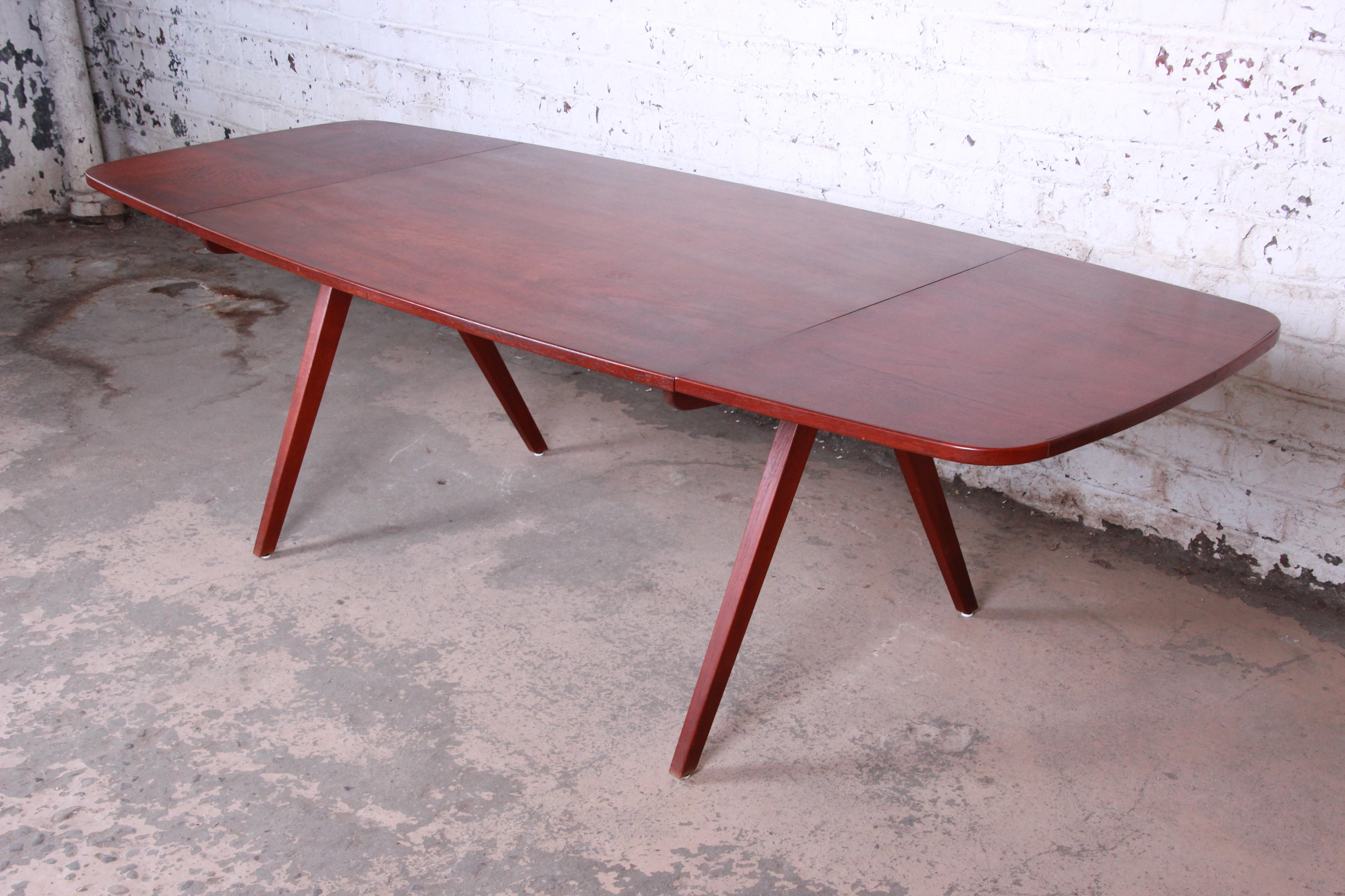 An outstanding Danish modern teak dining table designed by Poul Volther, circa 1950. The table features gorgeous wood grain and sleek, Minimalist midcentury Danish design. The boat-shaped top rests on unique solid teak scissor legs, and each end of