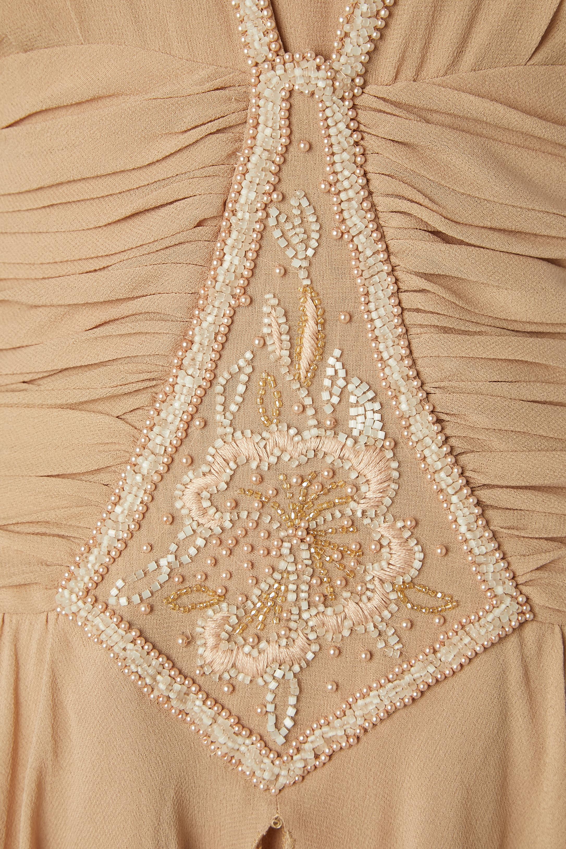 Abito da cocktail in chiffon di seta beige cipria con ricami di perline e fili. Drappeggiato in vita. Chiusura con zip nascosta e gancio sulla parte centrale della schiena + un bottone in tessuto e un'asola sulla parte centrale della schiena.