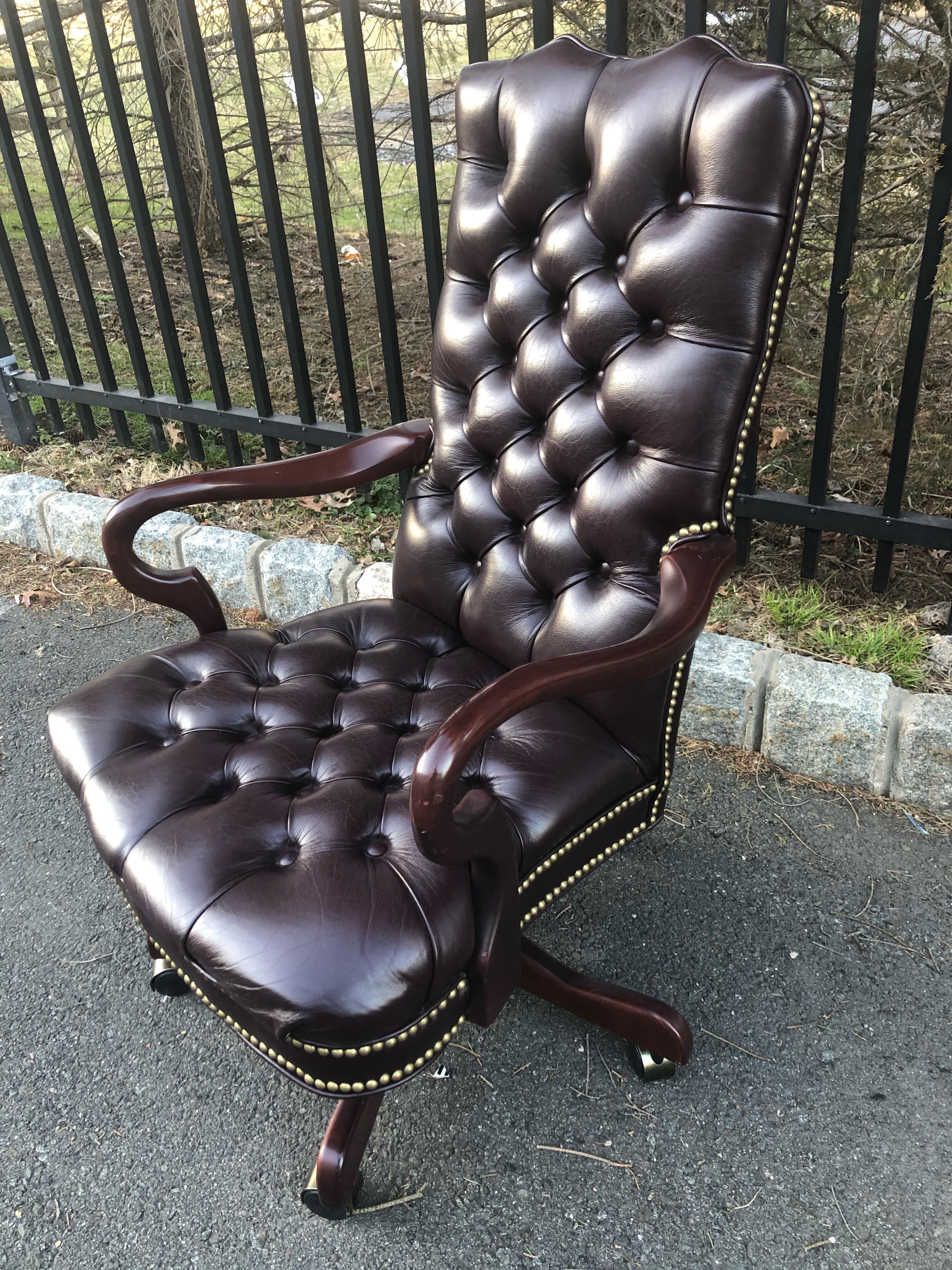 Luscious brown leather tufted desk chair with scroll wooden arms and nailhead trim. Chair is on casters and seat tilts and swivels. Color is a very dark burgundy which can pass for almost chocolate brown.