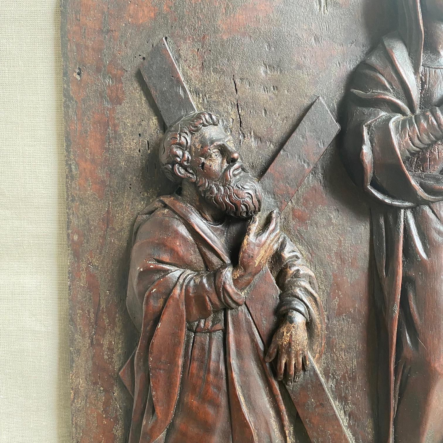 Aus einem einzigen massiven Walnussholzbrett geschnitzt, zeigt diese beeindruckende italienische Flachreliefplakette Maria mit dem Jesuskind, flankiert von zwei Aposteln, von denen einer ein Schwert und der andere ein Kruzifix hält. Die Figuren sind