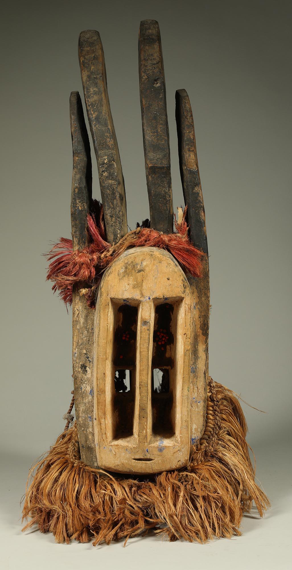 Cubist Dogon carved wood Antelope mask with attached raffia, from Mali West Africa. Tall vertical eyes, small slit mouth. Pair of carved curved blackened antelope horns rise from top of the head, long blackened ears.  With wonderful natural motion