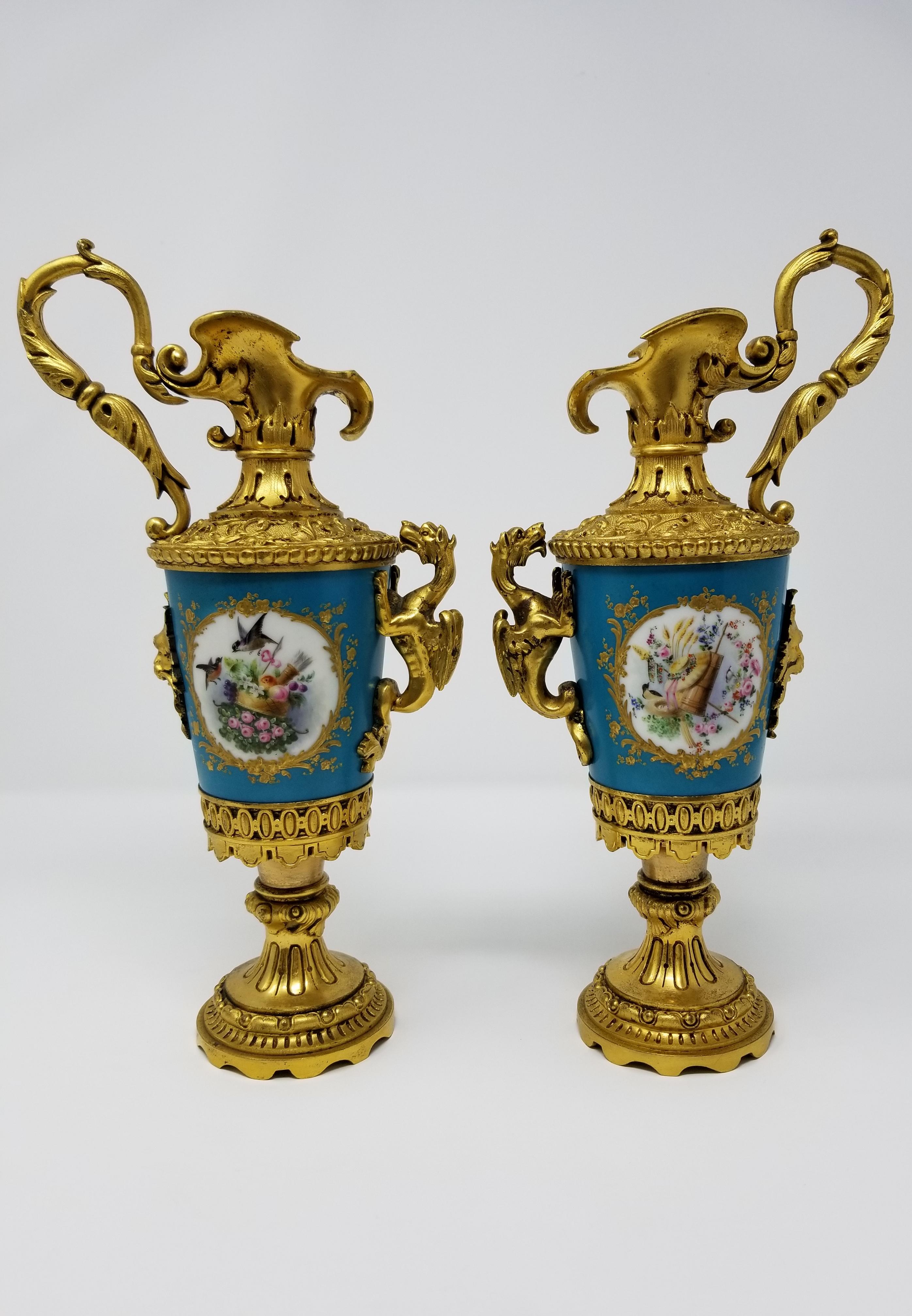 Une belle paire d'aiguières de style Louis XVI du 19ème siècle en porcelaine française de Sèvres et montées en bronze doré avec des poignées en forme de dragon, des oiseaux et des fleurs. La porcelaine est montée sur des montures en bronze Doré