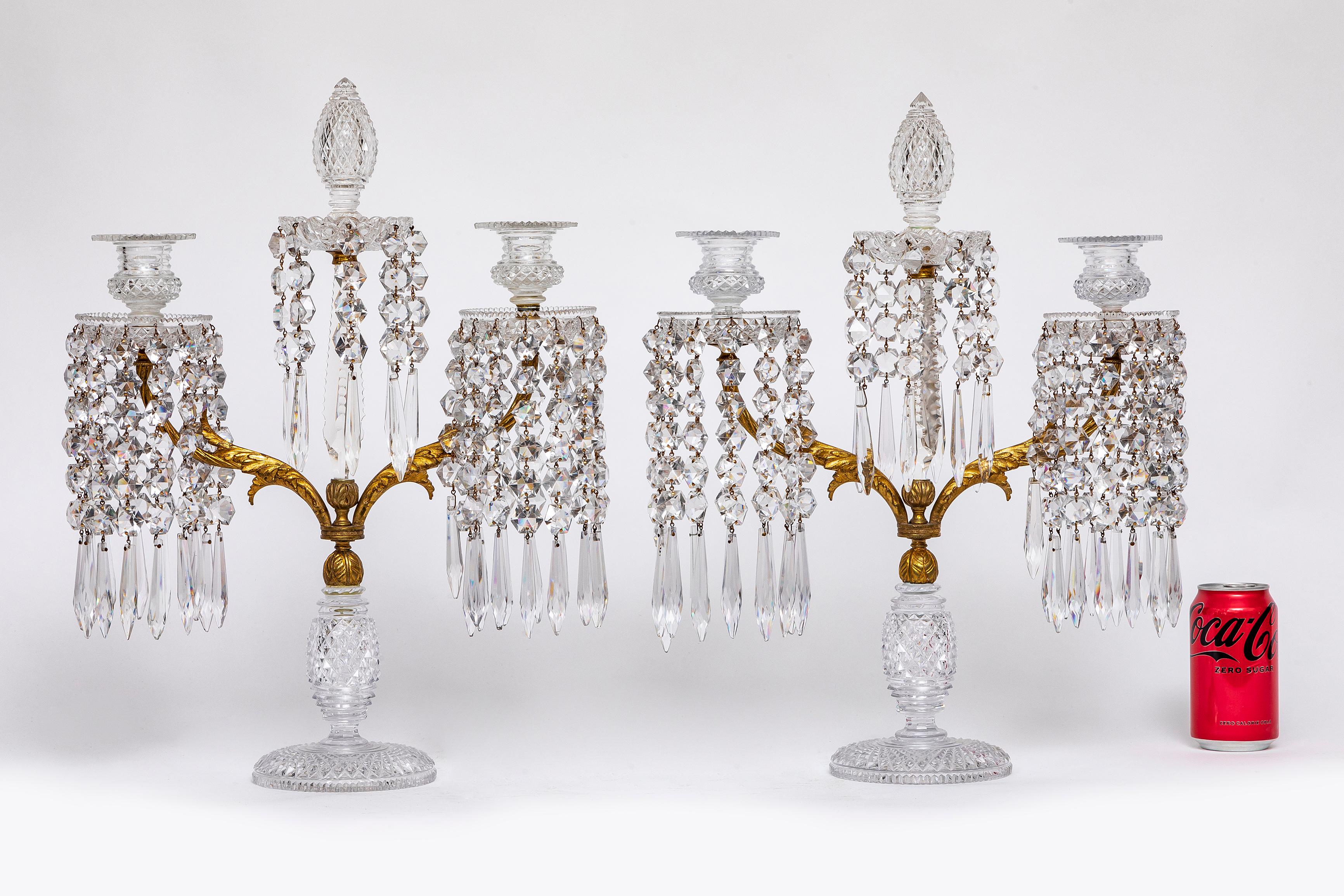 A Pair of Early 19th Century English Ormolu Mounted Hand-Diamond Cut Crystal Two-Arm Candelabra. Each candelabra features finely hand-diamond cut crystal elements mounted with ormolu detailing. Each is supported by a faceted crystal base with a