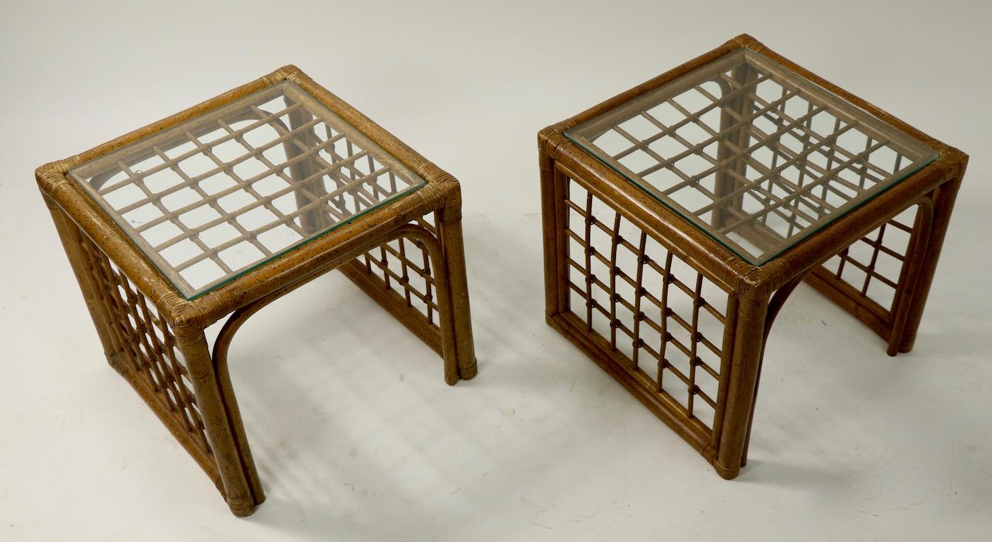 Chic pair of cube form bamboo stands with plate glass tops. Each table has cross hatch woven sides and open ends, both are in good condition, clean, sturdy, and ready to use. One glass top surface has been replaced, each stand shows minor cosmetic