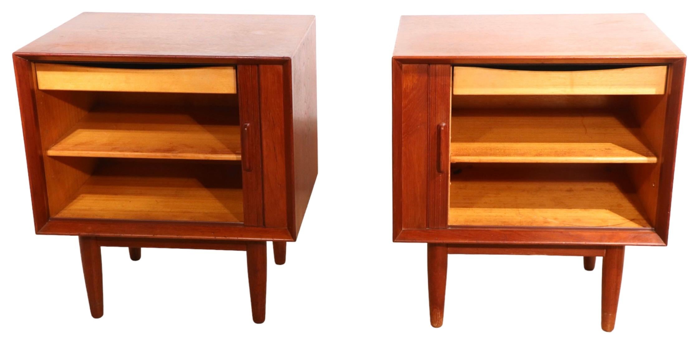 Architectural Danish Mid-Century Modern nightstands in teak, made in Denmark by Falster Mobelfabrik - circa 1950/1960’s.
The night tables feature a tambour roll front which opens to reveal a shelved storage bin, and an interior drawer. Both tables