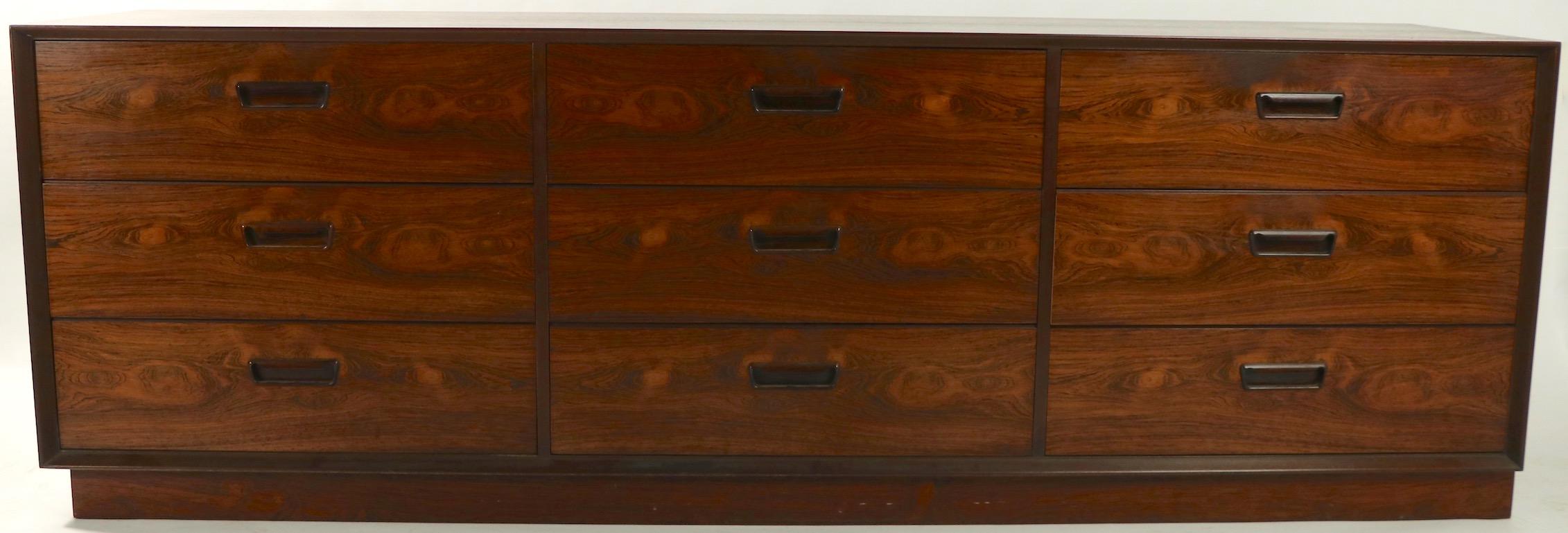 Stunning pair of large dressers made in Denmark for Dyrlund. Both are executed in rich and vibrant rosewood veneer, each having three banks of three drawers, with cutout inset pull handles. Very unusual to find a matched pair of dresser, credenza,