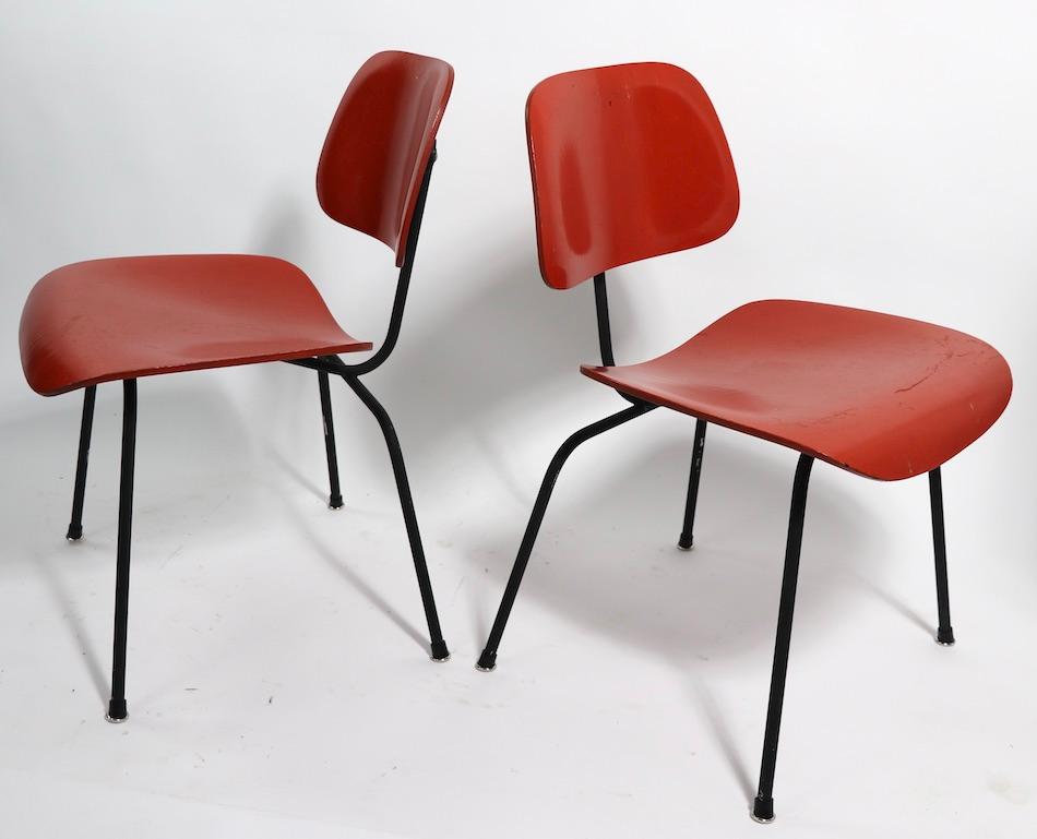 Pair of Eames designed DCM (Dining Chair Metal). Chairs This pair of chairs are currently in later, but not new, orange paint finish, the metal frames are also in later black paint finish, and the feet glides are later replacements. While the paint