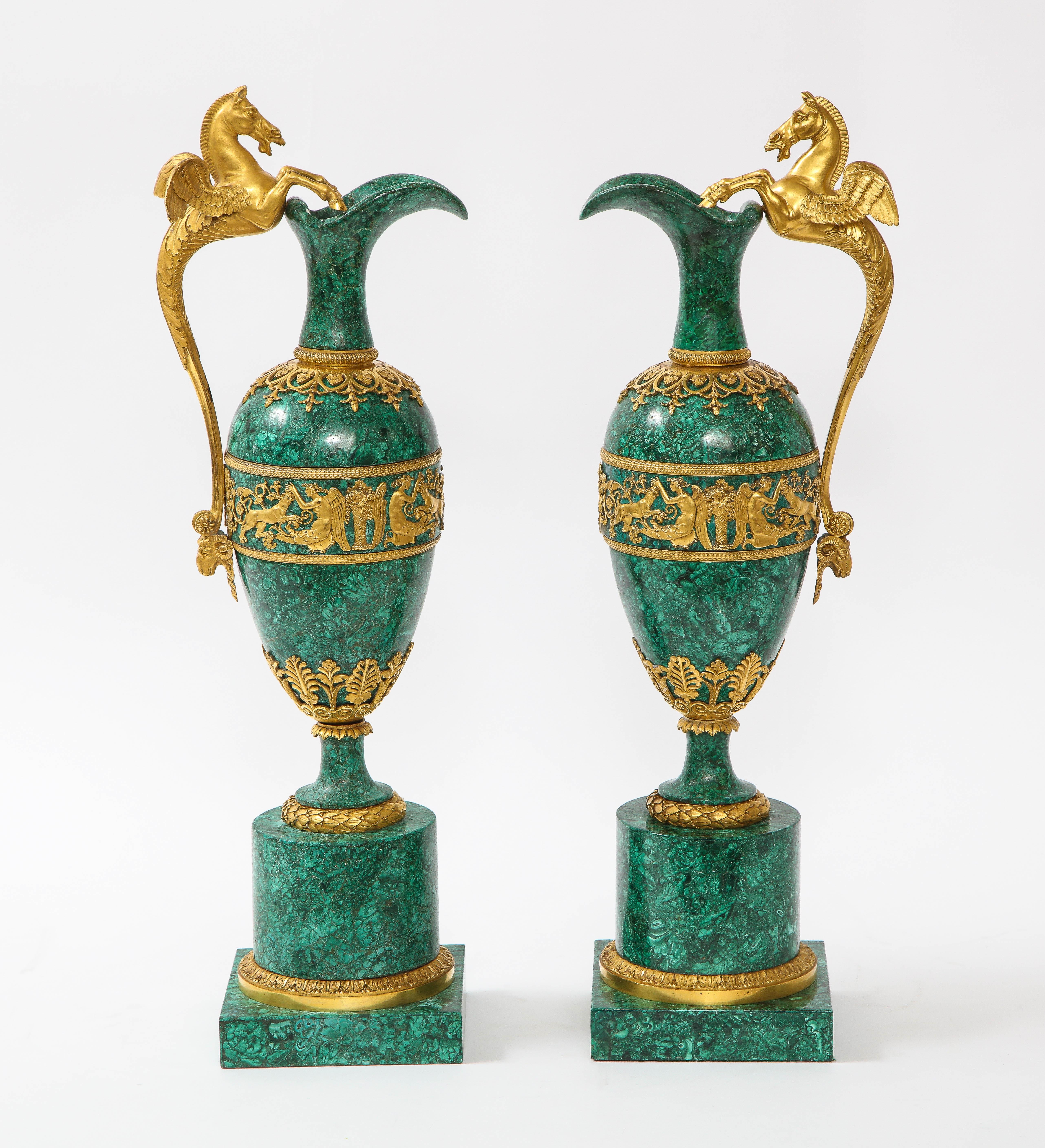 A pair of Empire Ormolu-Mounted Malachite Ewers attributed to Claude Galle, circa 1805, Possibly Made For The Russian Market. Each with an ovoid body applied with an ormolu band depicting winged figures feeding with panthers, the top and base with