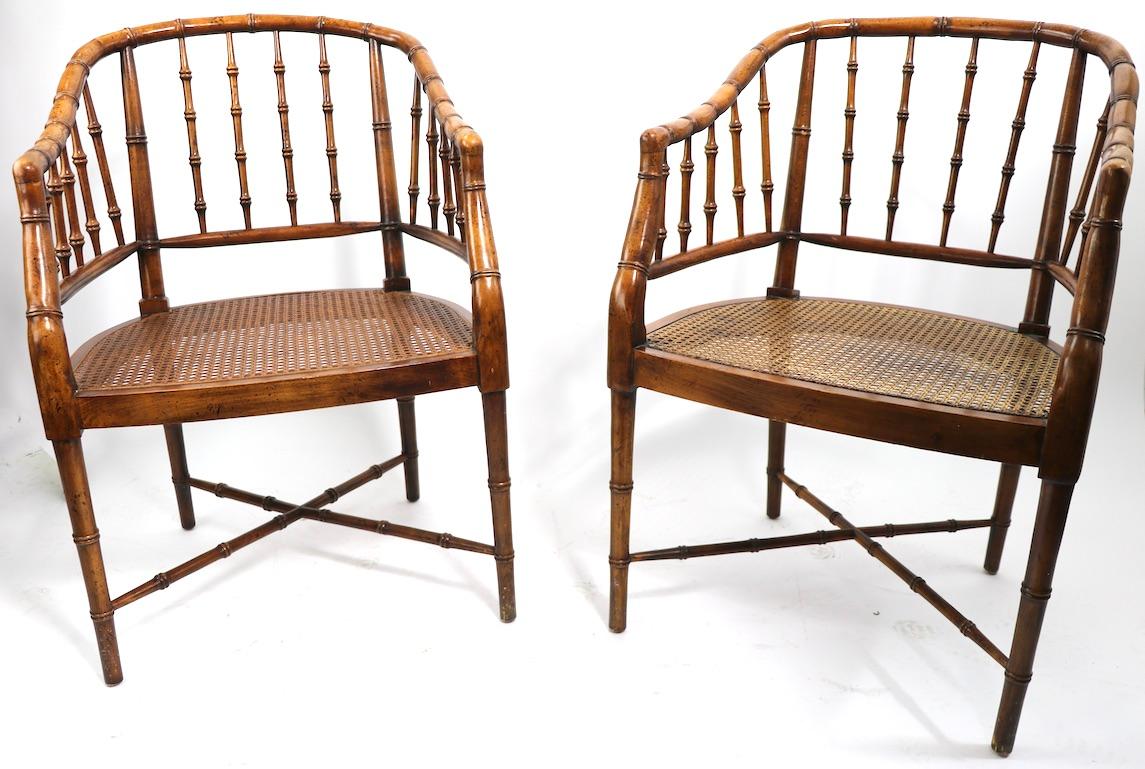 Voguish and chic style pair if faux bamboo barrel back lounge chairs, having solid wood frames and caned seats. Both are in very fine, original condition, free of breaks, damage or repairs. Offered and priced as a pair, one chair has remnants of a