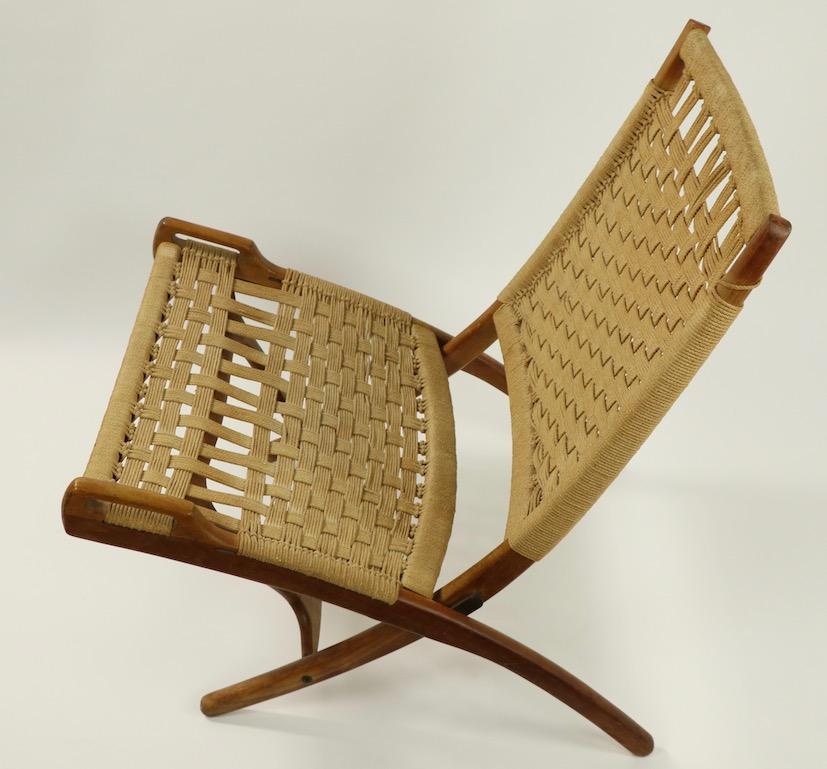 Pair of chic architectural folding scissor chairs made in Italy after the original Wegner design. These chairs have solid wood frames, woven rope seats and backs, and brass hardware. Both are in overall very good, original condition, one shows