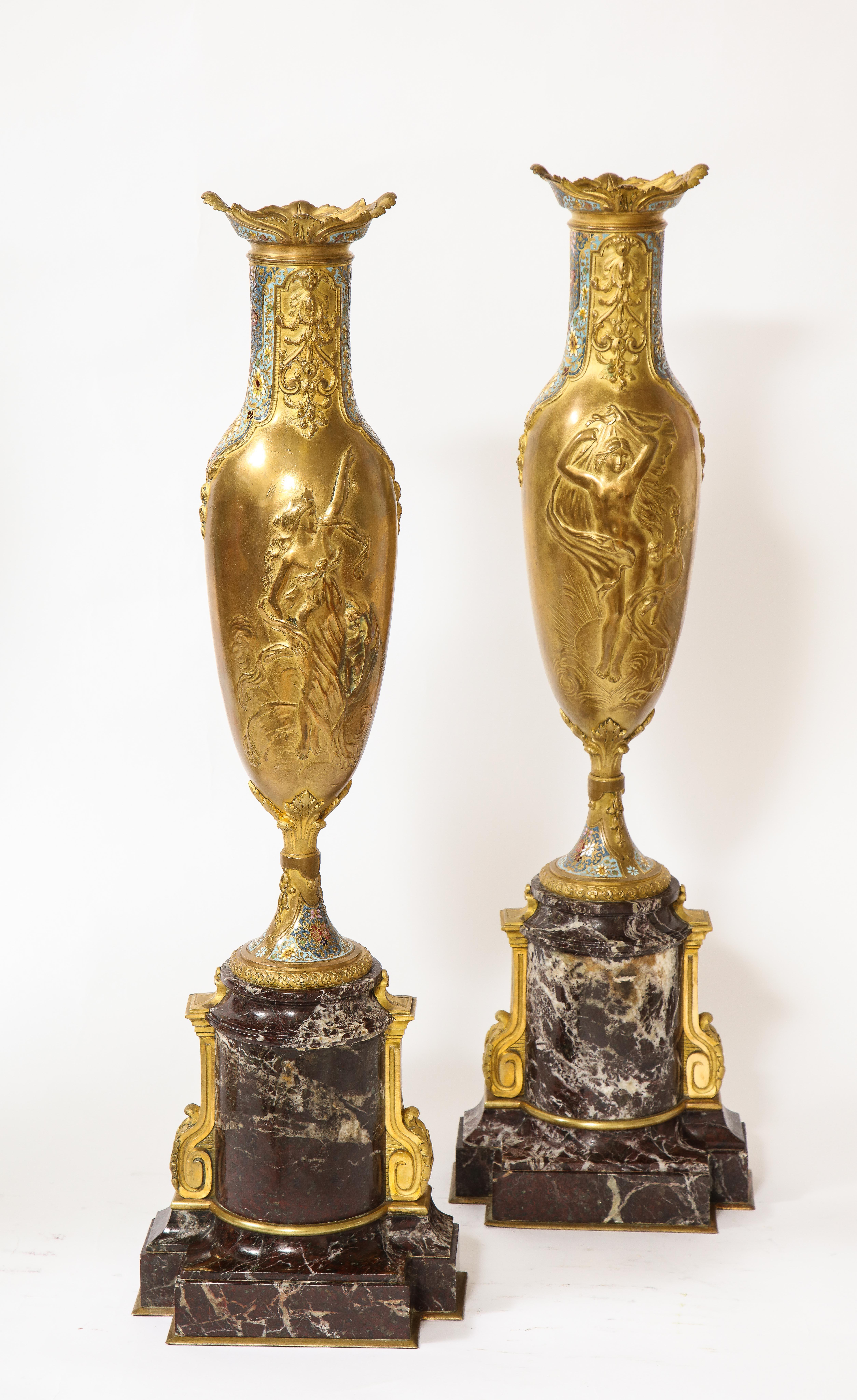 A Pair of French 19th century Louis XVI style Dore bronze, Champlevé Enamel, and rouge marble mounted 'Day and Night' Vases. Each vase is beautifully cast, hand-chased, and hand-chiseled with meticulous detail. On each of the vases are relief images