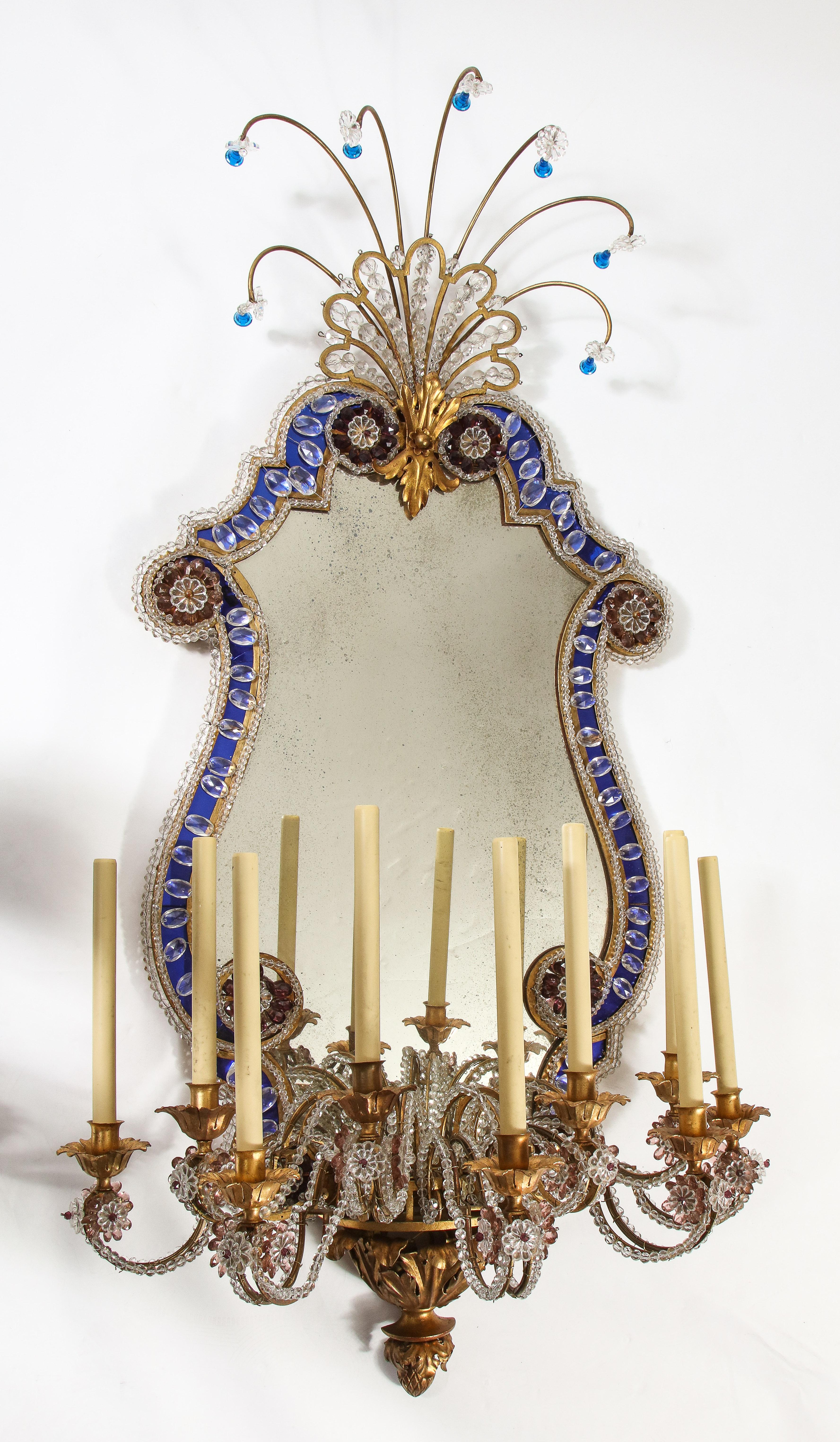 A monumental pair of antique french 20th century dore bronze mounted mirrored and breaded crystal nine-arm sconces attributed to Baguès. Each sconce is beautifully decorated with an antique mirrored back, which is encased in a blue crystal boarder,