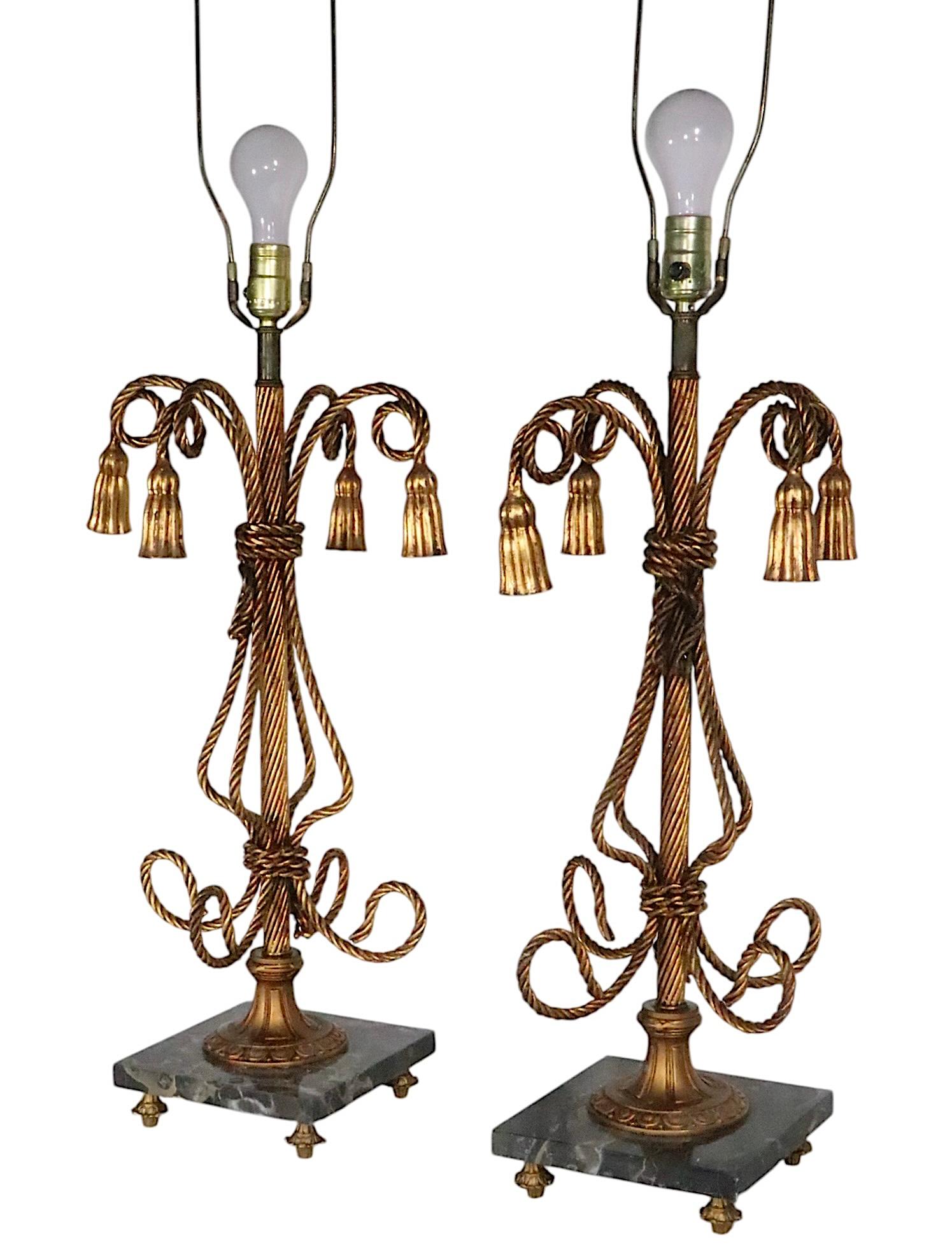 Coppia di eleganti oggetti in metallo dorato, realizzati in Italia negli anni 1950/60 circa. 
Lampade da tavolo in stile Hollywood Regency, Palm Beach, con corpi stilizzati in corda e nappe, con basi quadrate in marmo, su piedi in metallo. Abbiamo
