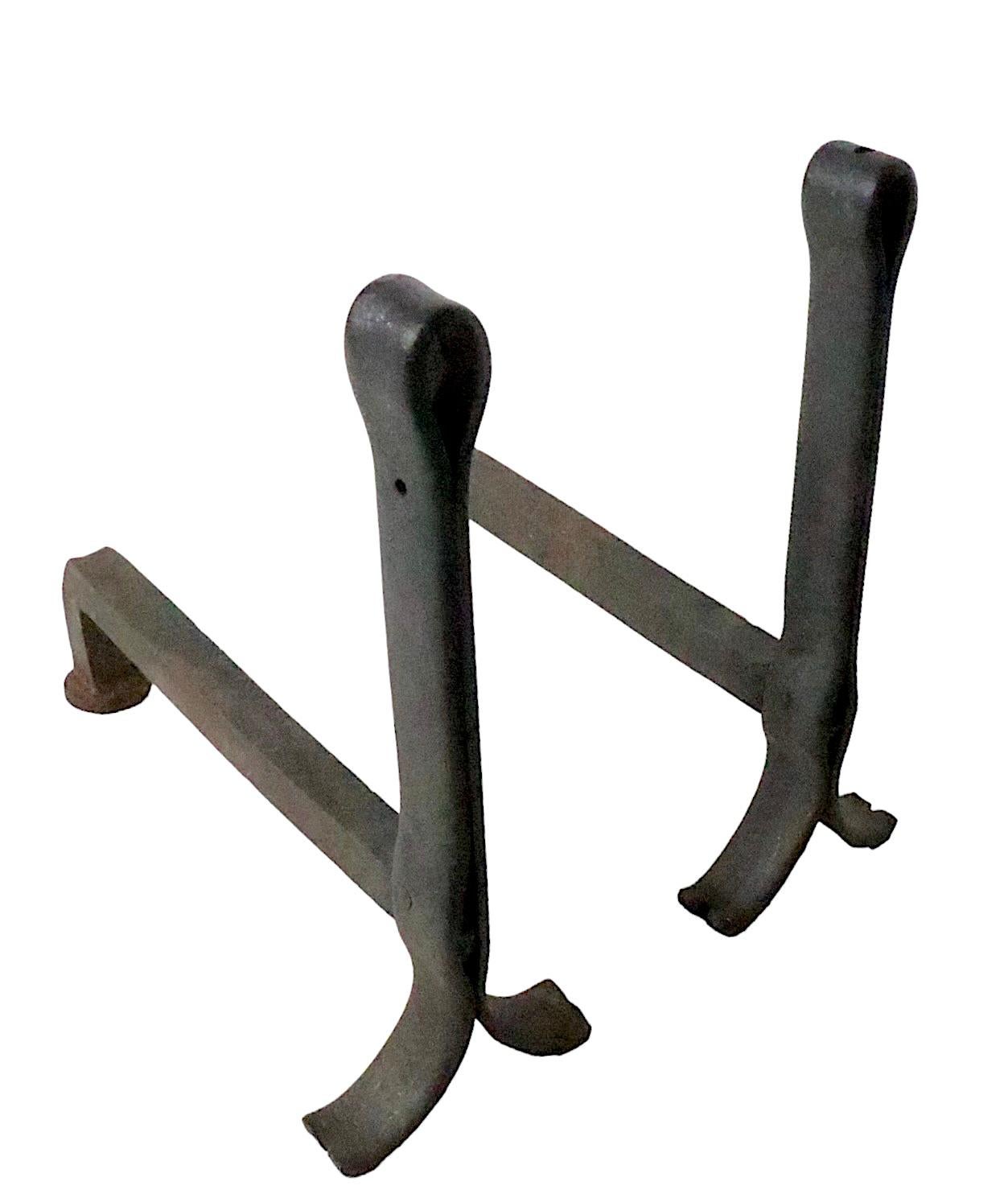 Chic architectural andirons of heavy had forged iron, possibly constructed of old railroad ties.
The pair features a simple loop form top, which creates a spare graphic and modernist look, suitable for both traditional, mid century, and