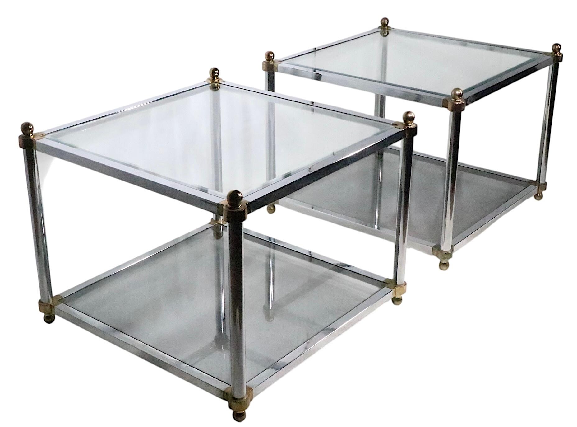 Pair of chic Hollywood Regency style side, or end, tables having chrome plated frames and brass plated joinery. The tables have  two bevelled glass shelves, the top being transparent the bottom tinted. Reminiscent of Maison Jansen, and Milo