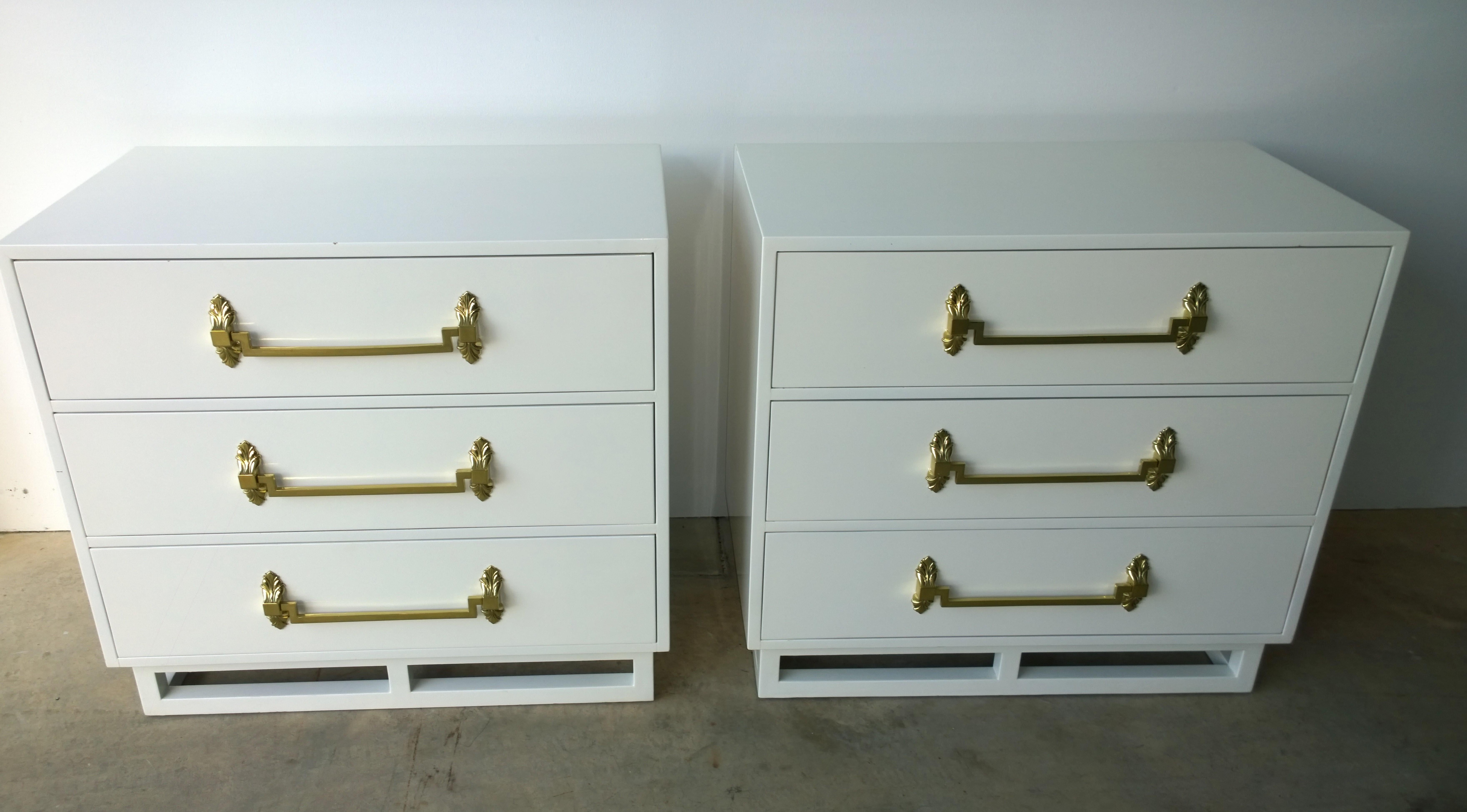 Offered is a pair of Hollywood Regency or Mid-Century Modern signed Grosfeld House lacquered wood in white with brass decorative hardware chest of drawers / night tables / dressers. The pair sit on an open lacquered wood plinth base. This gorgeous
