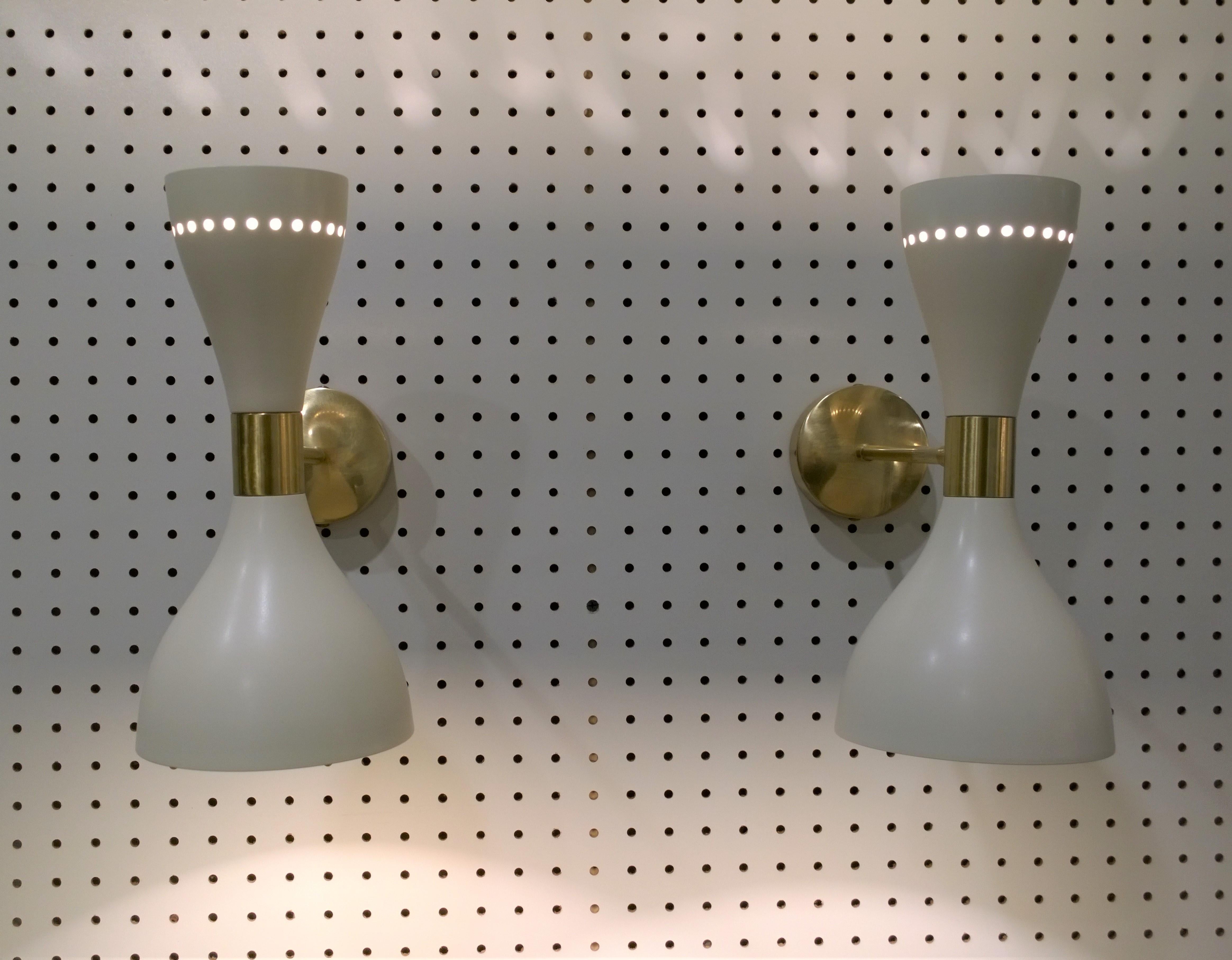 Offered is a pair of Italian mid century modern Stilnovo style white enameled metal and brass accents sconces.  Beyond gorgeous and quite on trend.  This pair will need to be rewired for U.S. standards.  We do not warranty or accept liability for