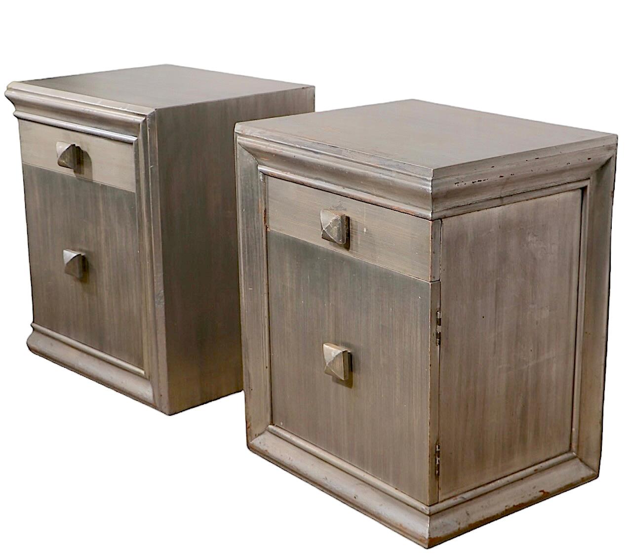 Voguish pair of Hollywood Regency night tables designed by James Mont. The nightstands feature an asymmetrical molding frame with one drawer over a door, which opens to reveal open storage. The cases are in silver gilt finish, the interior storage