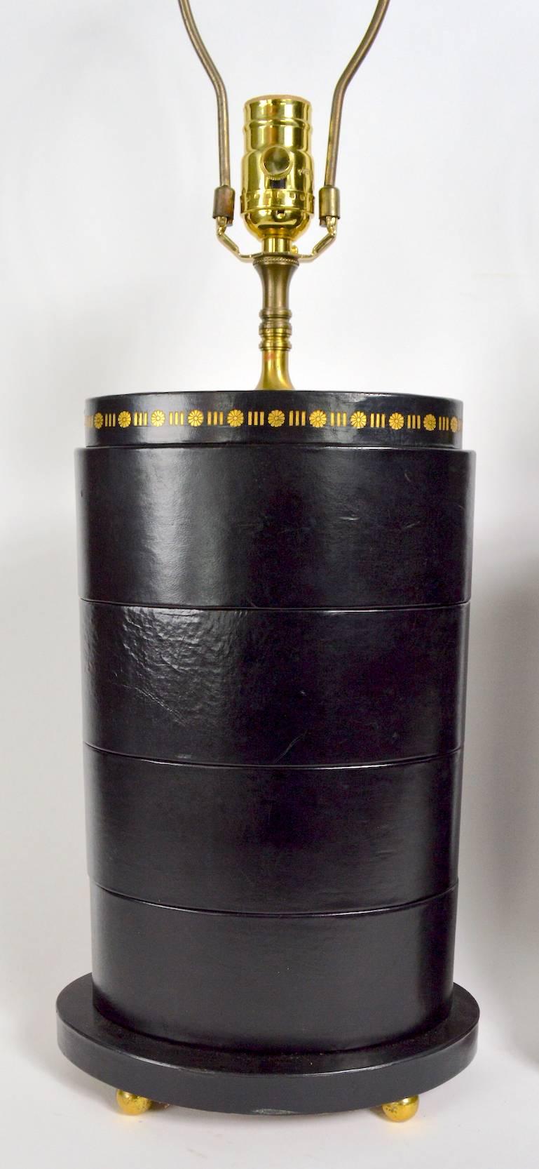Pair of chic black leather wrapped stacked oval table lamps. These lamps are in fine working condition, both show minor cosmetic wear, normal and consistent with age (damage pictured). Height to top of leather body 13.75 inches.