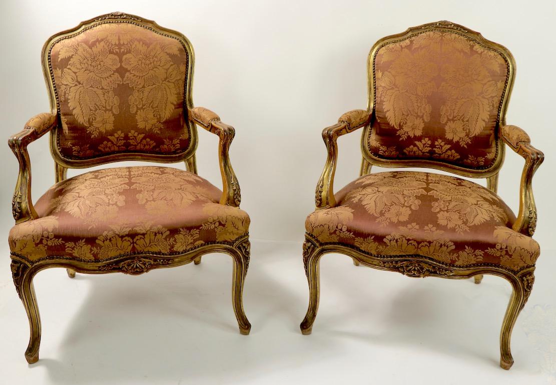 Stylish pair of giltwood and upholstered fauteuil chairs in the Louis LV style. Both chairs are structurally sound and sturdy, however the fabric shows wear, please see images. We believe these chairs are early to mid-20th century vintage, however