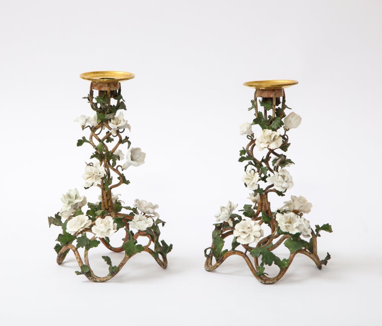 An exquisite pair of 18th century Louis XV Period French patinated tole and gilt bronze candle sticks embellished with white porcelain flowers. This is truly an unusual and beautiful pair of candle sticks. Each has a beautiful swirling design made