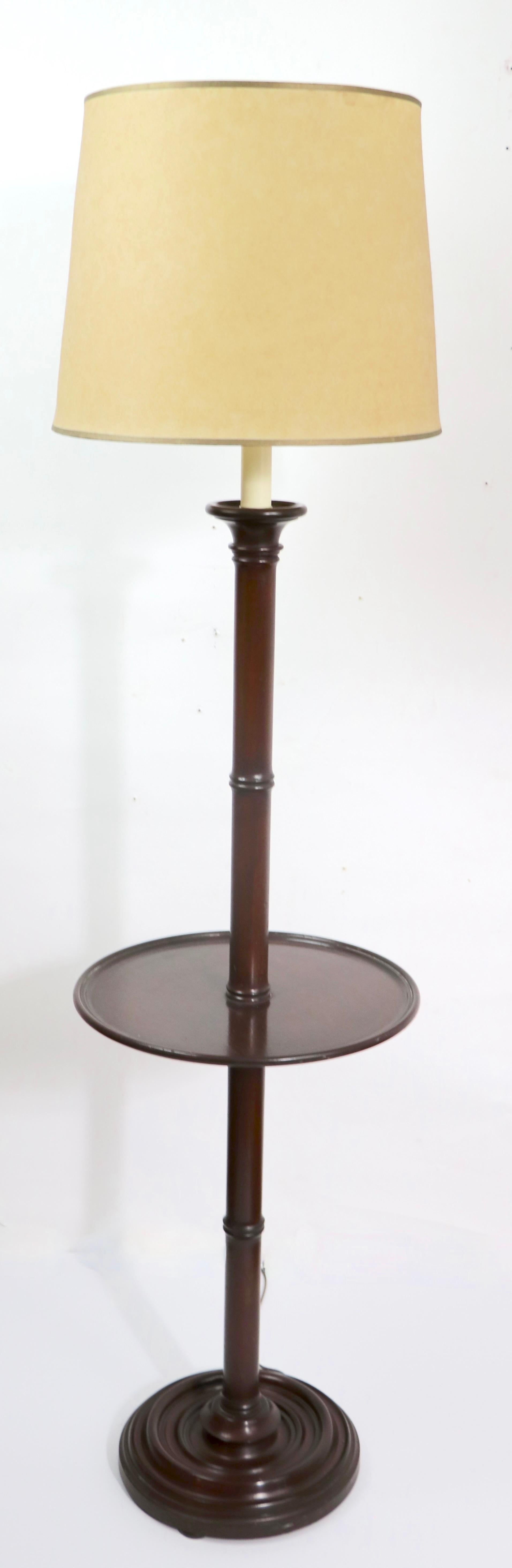 Stylish pair of floor lamp/ tables having a turned wood center pole with circular table surface incorporated in the middle of the lamp. Table surface 15 inch Dia. Total H 61 x H to top of wood 52 inch - Constructed of solid mahogany.
 Clean,