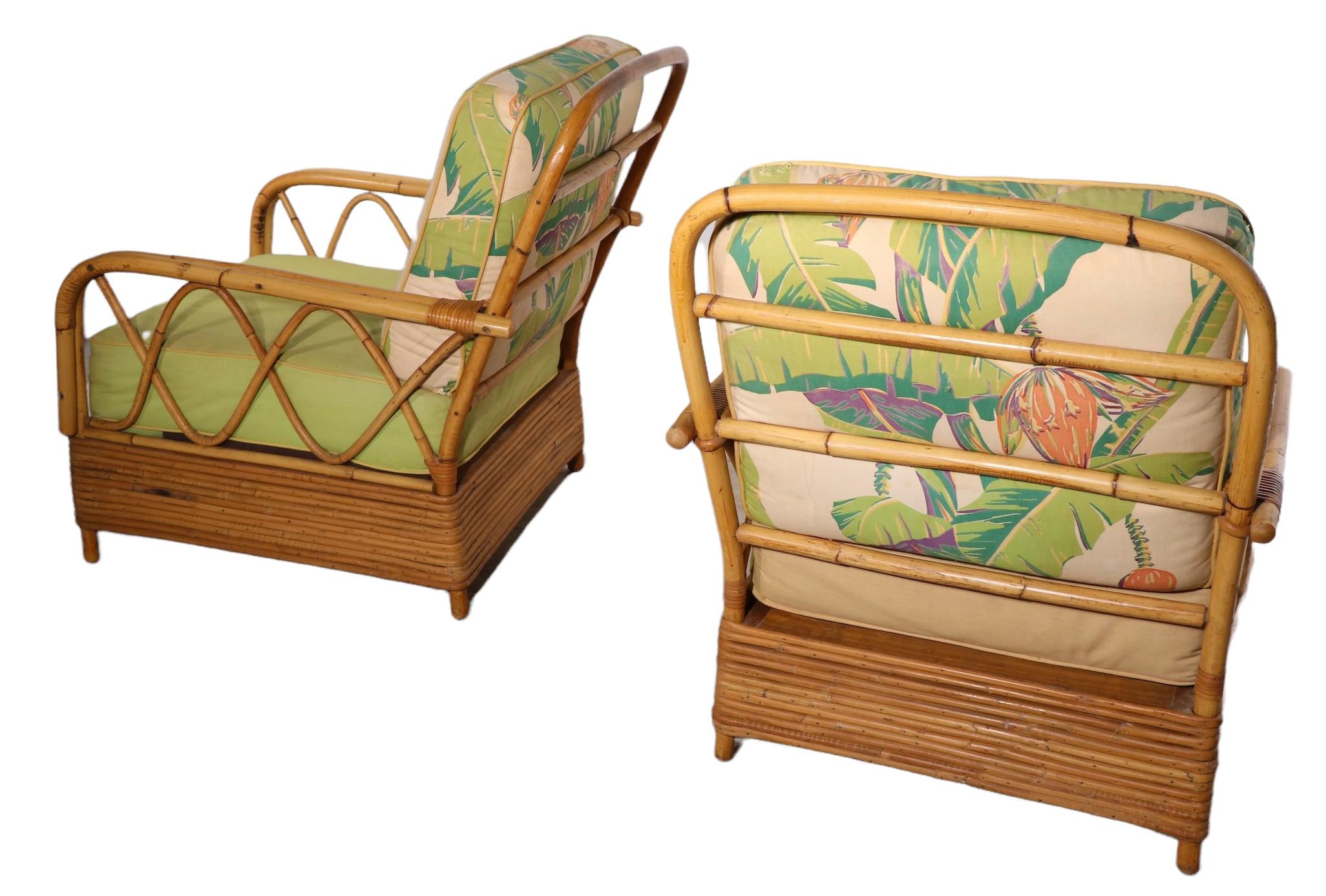 Voguish, chic pair of mid century lounge, club chairs by noted American furniture maker Ficks Reed. These chairs feature a plinth like banded bamboo base, with bent bamboo arms and back. The cushions are in original tropical floral print, usable as