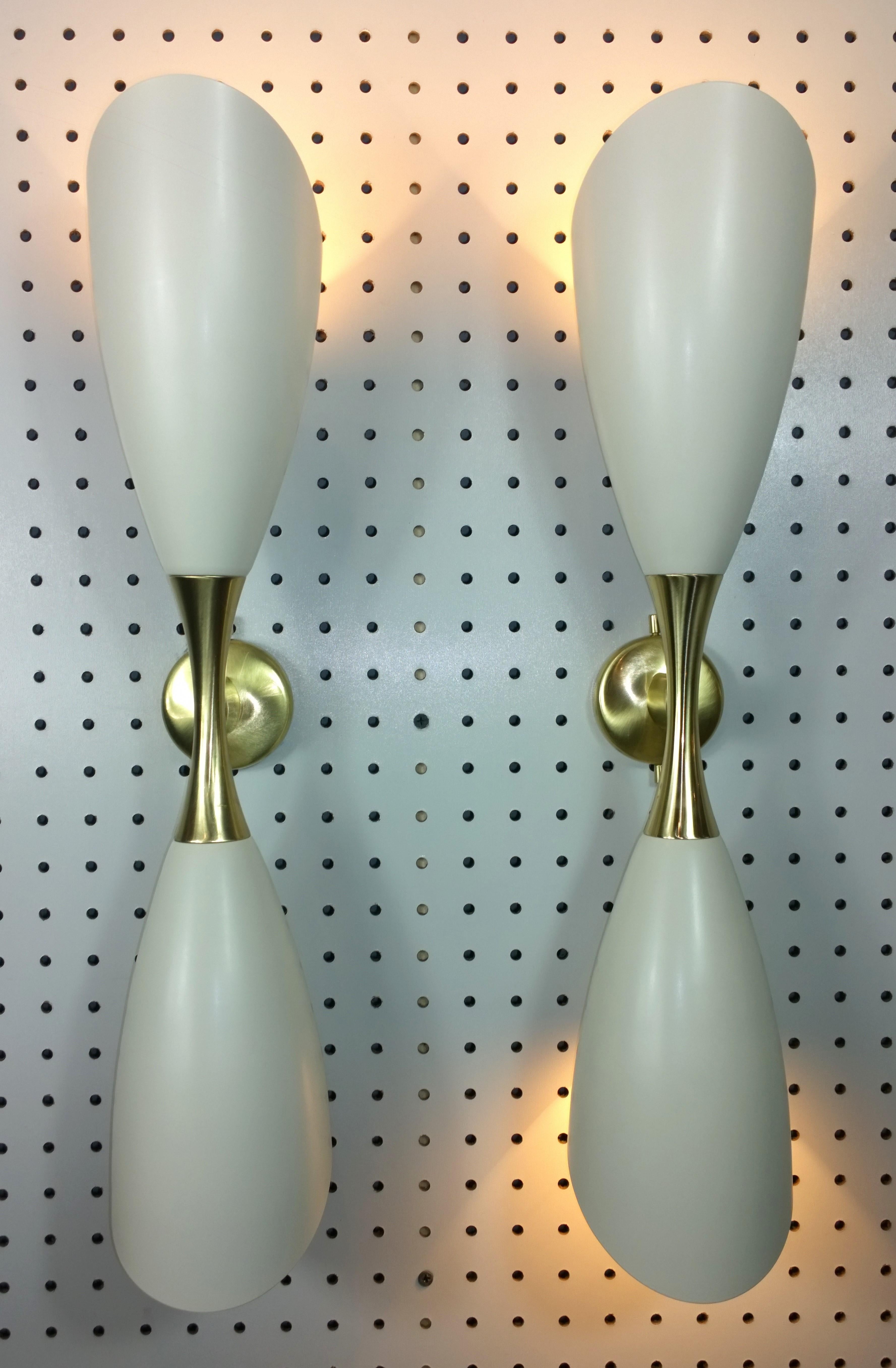 Offered is a pair of Mid-Century Modern Italian Stilnovo style white enameled aluminum elongated double cone with brass accented hardware sconces. These Italian enameled sconces were produced in the 1950s-1960s and are vintage and not new production