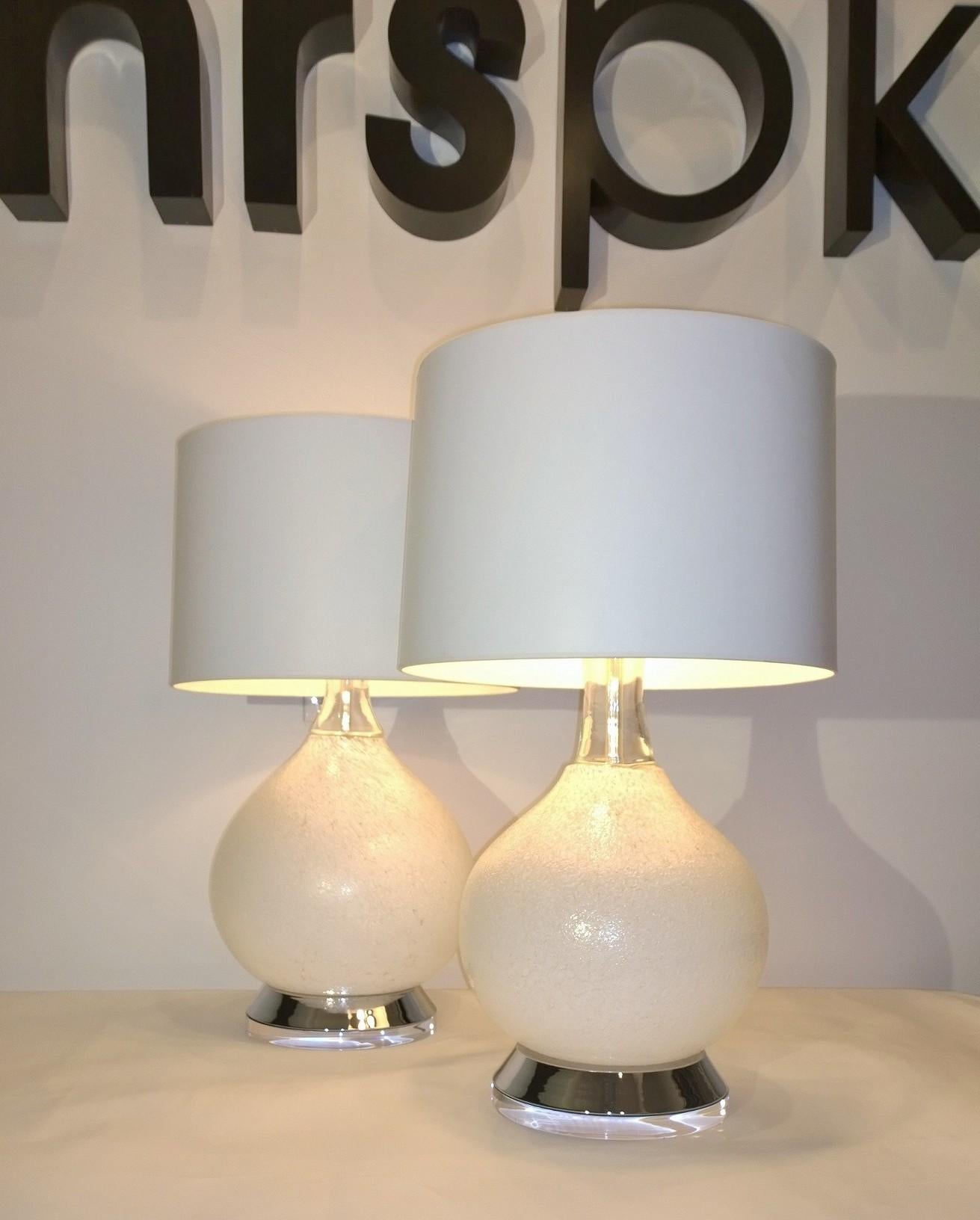 Offered is a pair of Mid-Century Modern Italian Vistosi white textured and clear Murano glass with chrome and Lucite base table lamps. The round surface of the lamp is flecked in white which adds an extra wow with the chrome flared base with thick