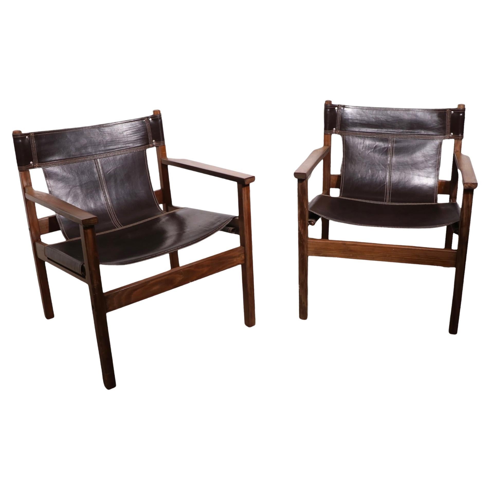 Chic pair of mid-century safari chairs, in original brown leather and wood. Both chairs are in very fine, original, clean and ready to use condition. Hard to find nice vintage pairs still intact. Design reminiscent of Michael Arnoult, unsigned. 

