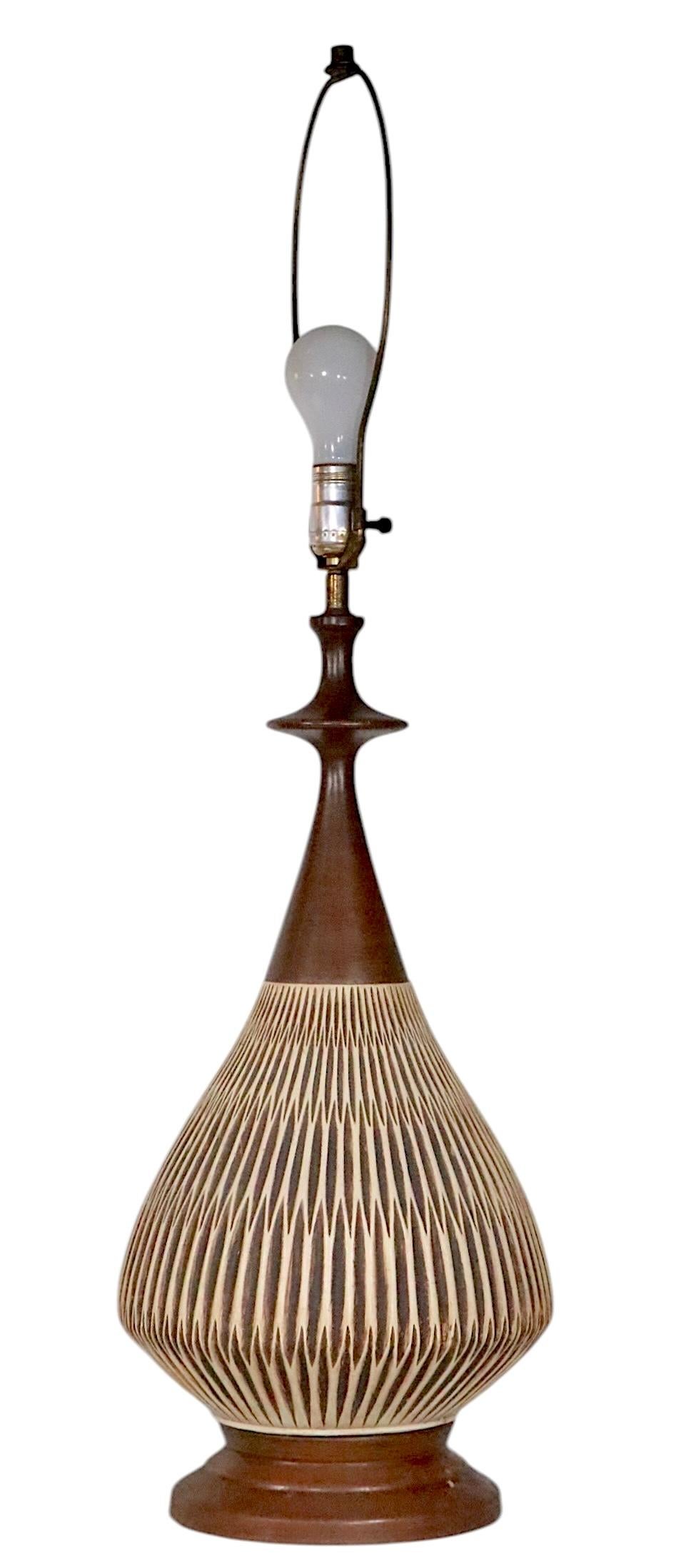 Impressive, large scale pair of mid century table lamps, having bulbous ceramic bodies, with  dimensional ribbed surfaces,  and faux wood finished metal bases and tops. Both are in good, original, working condition, showing minor cosmetic wear,