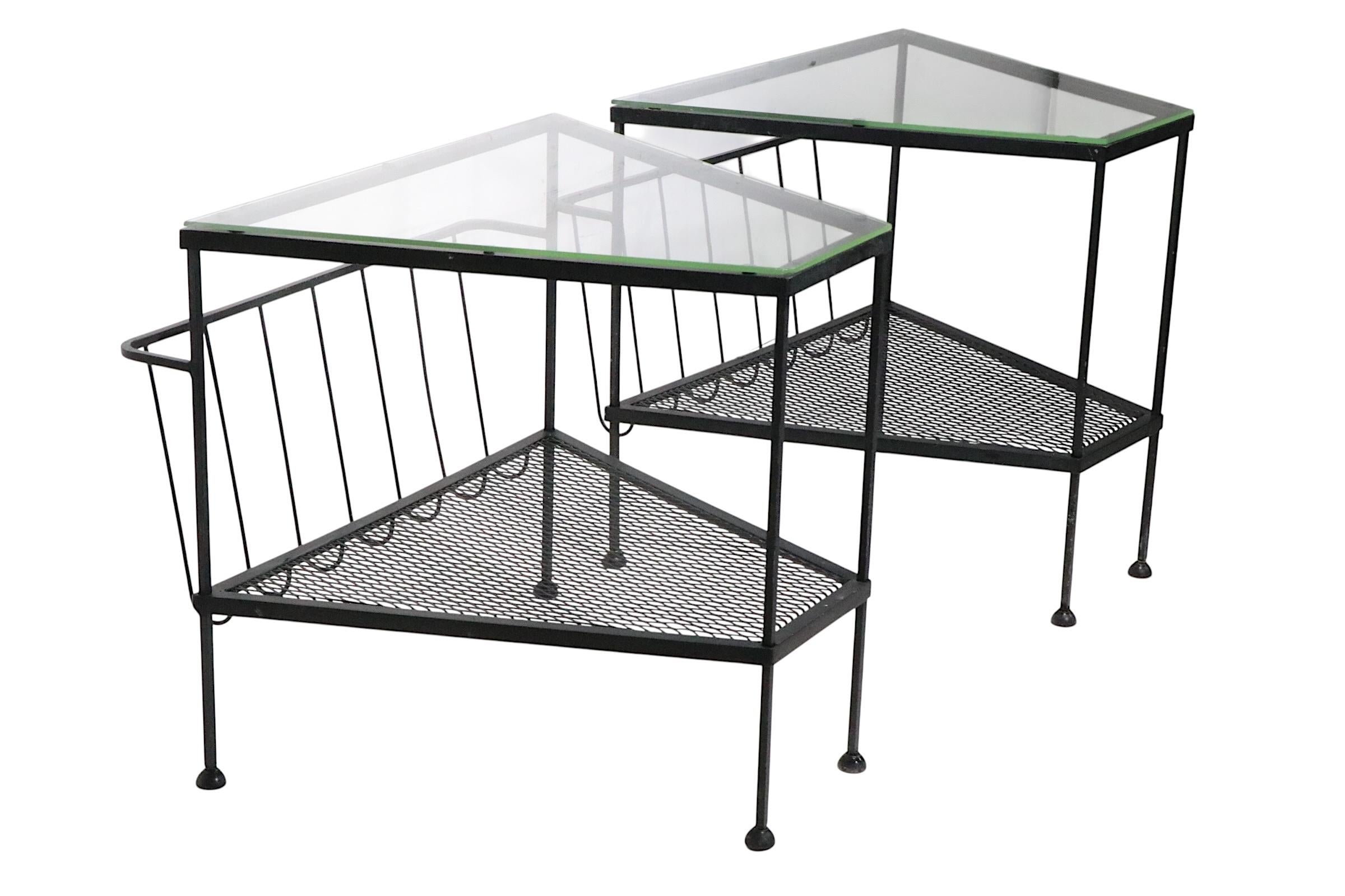 Pair of architectural mid century end tables made in the USA, by the Troy Sunshade Company, circa 1950/60's. The tables feature wedge form glass tops, a metal mesh lower shelf, and a magazine rack. Both stands are structurally sound and sturdy, both