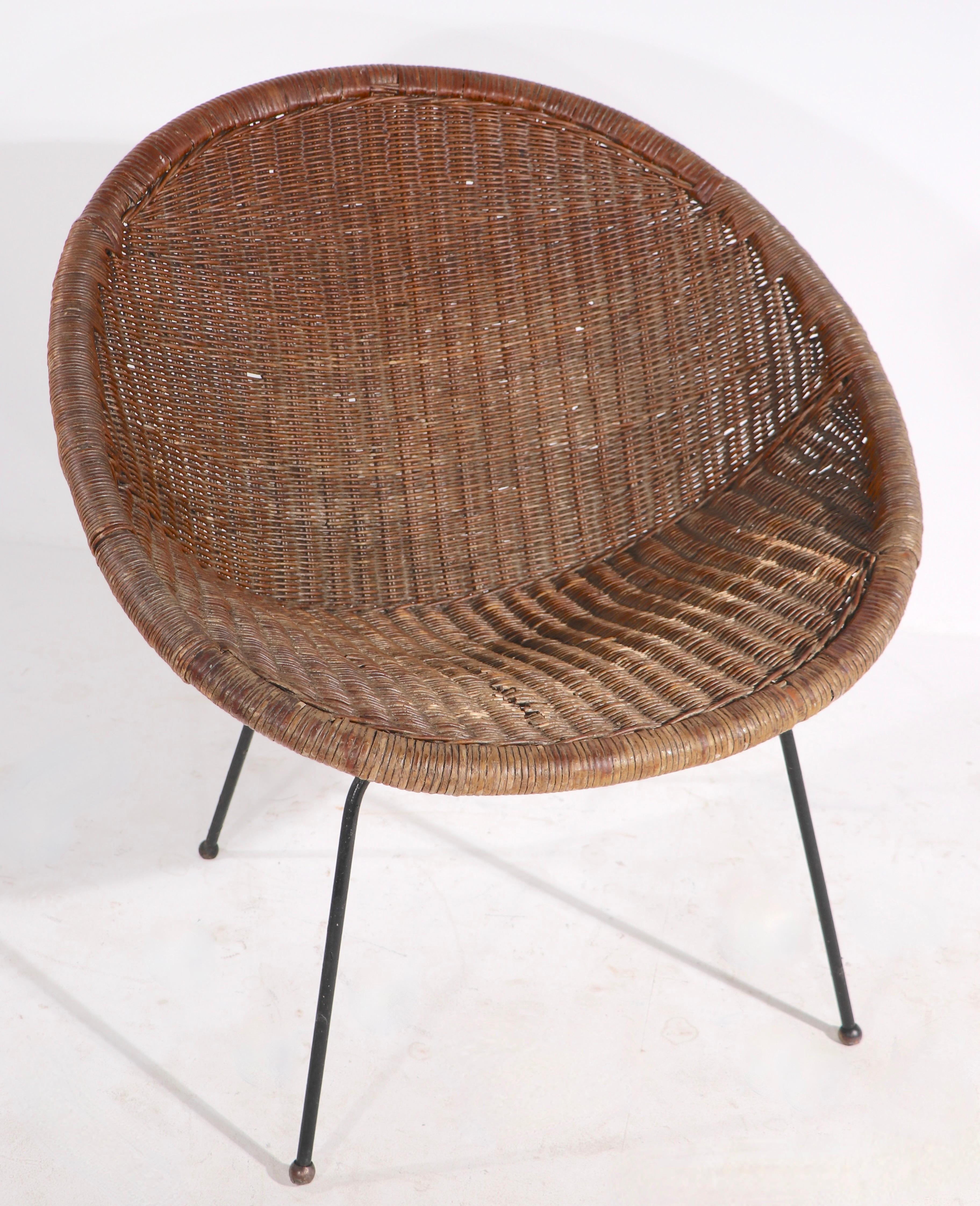 Pair of mid century woven wicker lounge chairs on wrought iron legs. Both chairs are in good, original condition, both show some wear, and minor loss to the wicker, one chair is missing one ball foot. Offered and priced as a pair.
